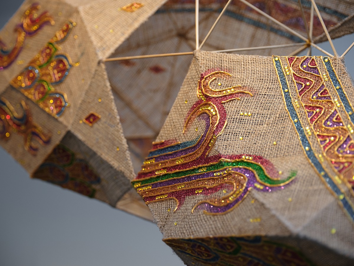 A closeup of a sculpture cnstructed of woven fibre and bambbo sticks with colourful stylised symbols painted on it