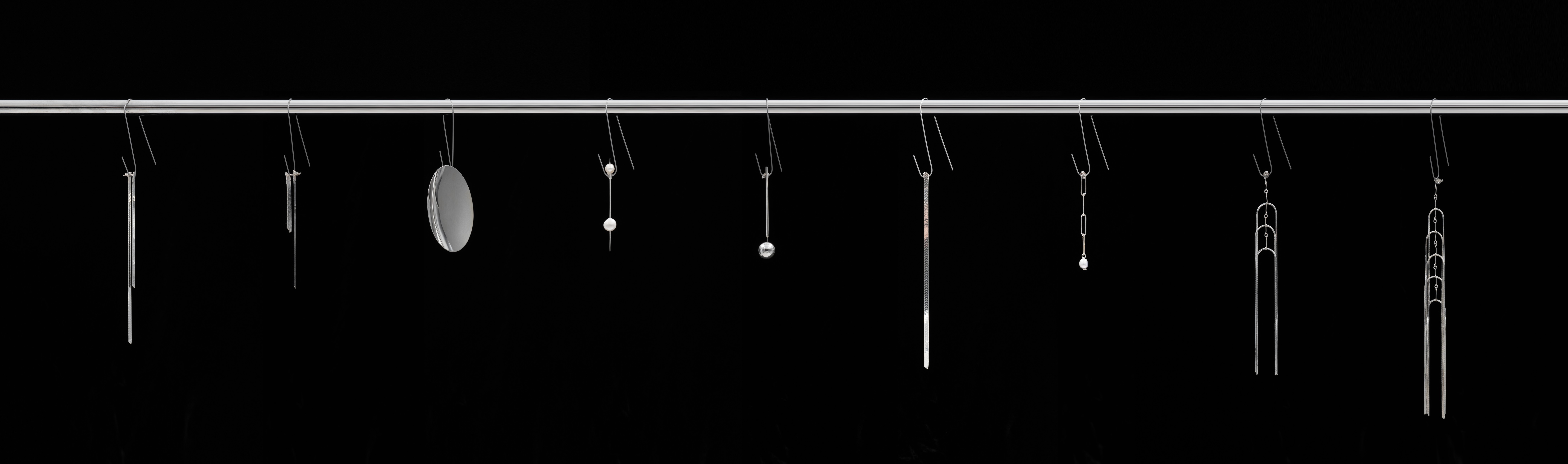 A range of different earrings hanging from a slender silver pole against a black backdrop