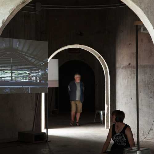 Inside concrete silos a video work plays on a screen while a seated person watches.