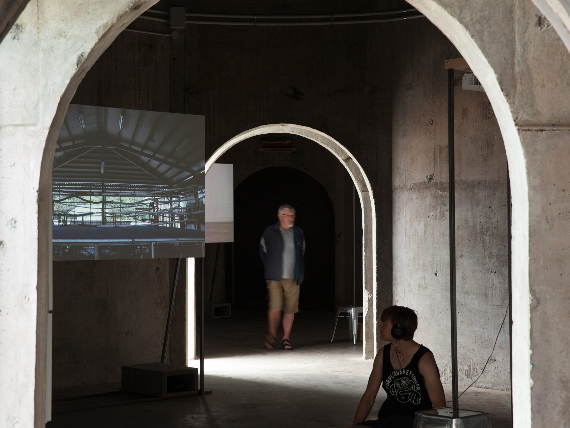 Inside concrete silos a video work plays on a screen while a seated person watches.