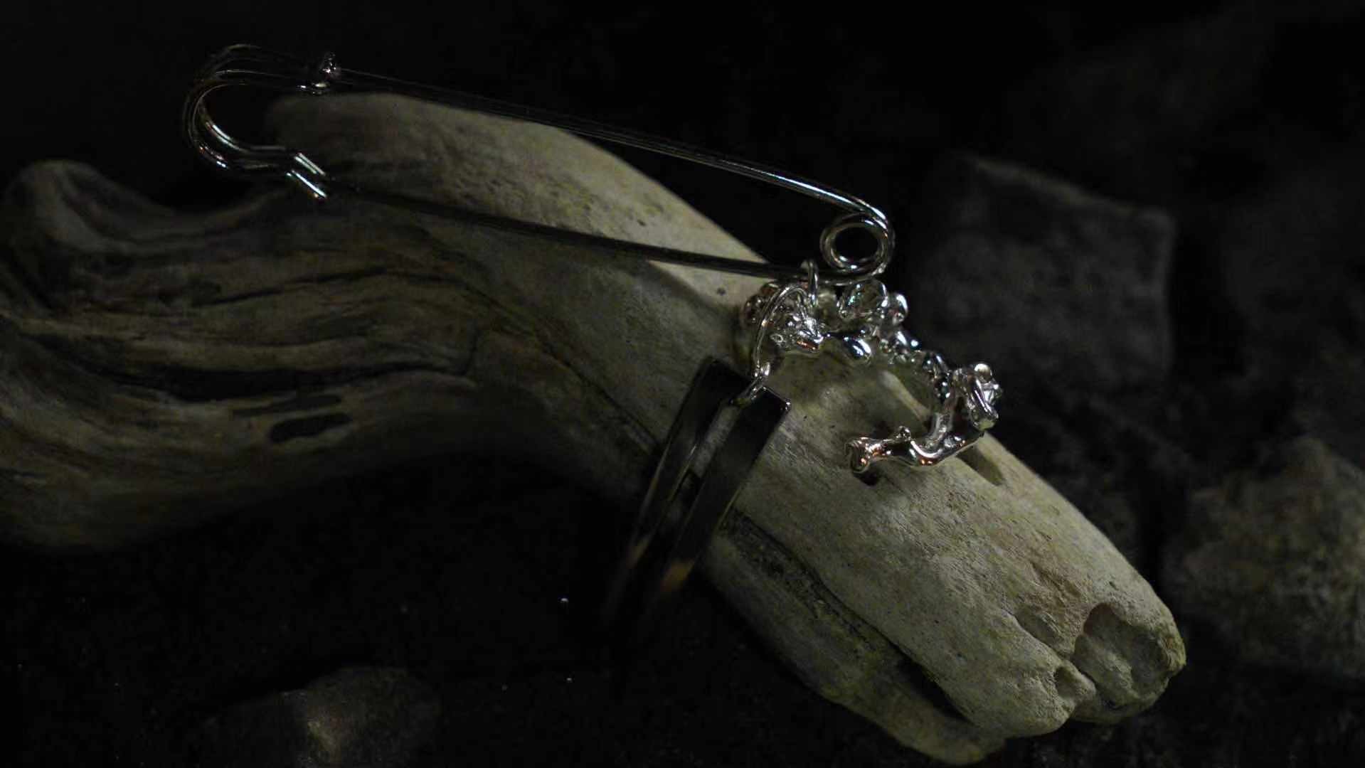 A safety pin with a free-form silver shape attached, which in turn is attached to a cuff that is wrapped around a piece of driftwood