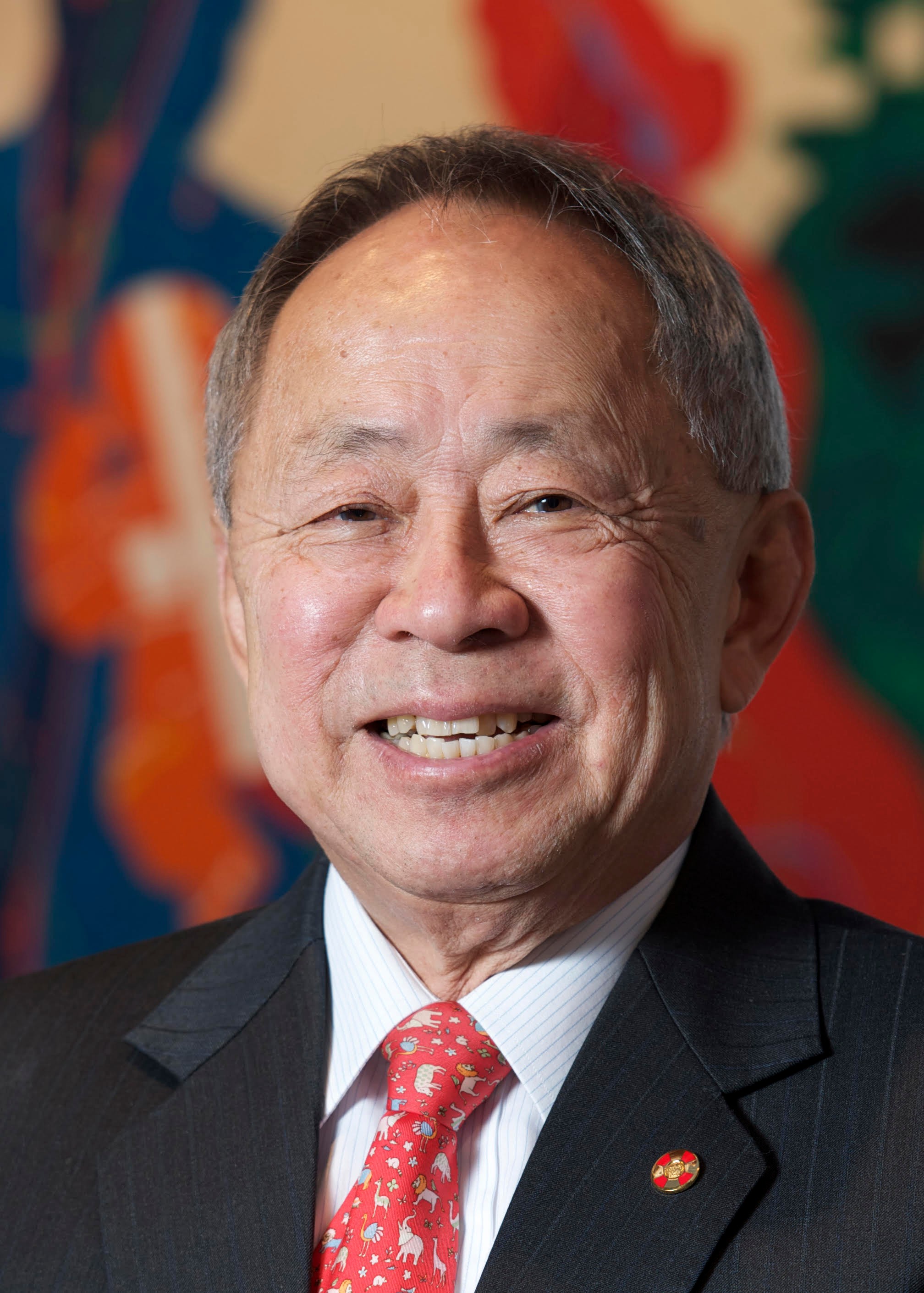 A photographic portrait of a man smiling wearing a suit and red tie