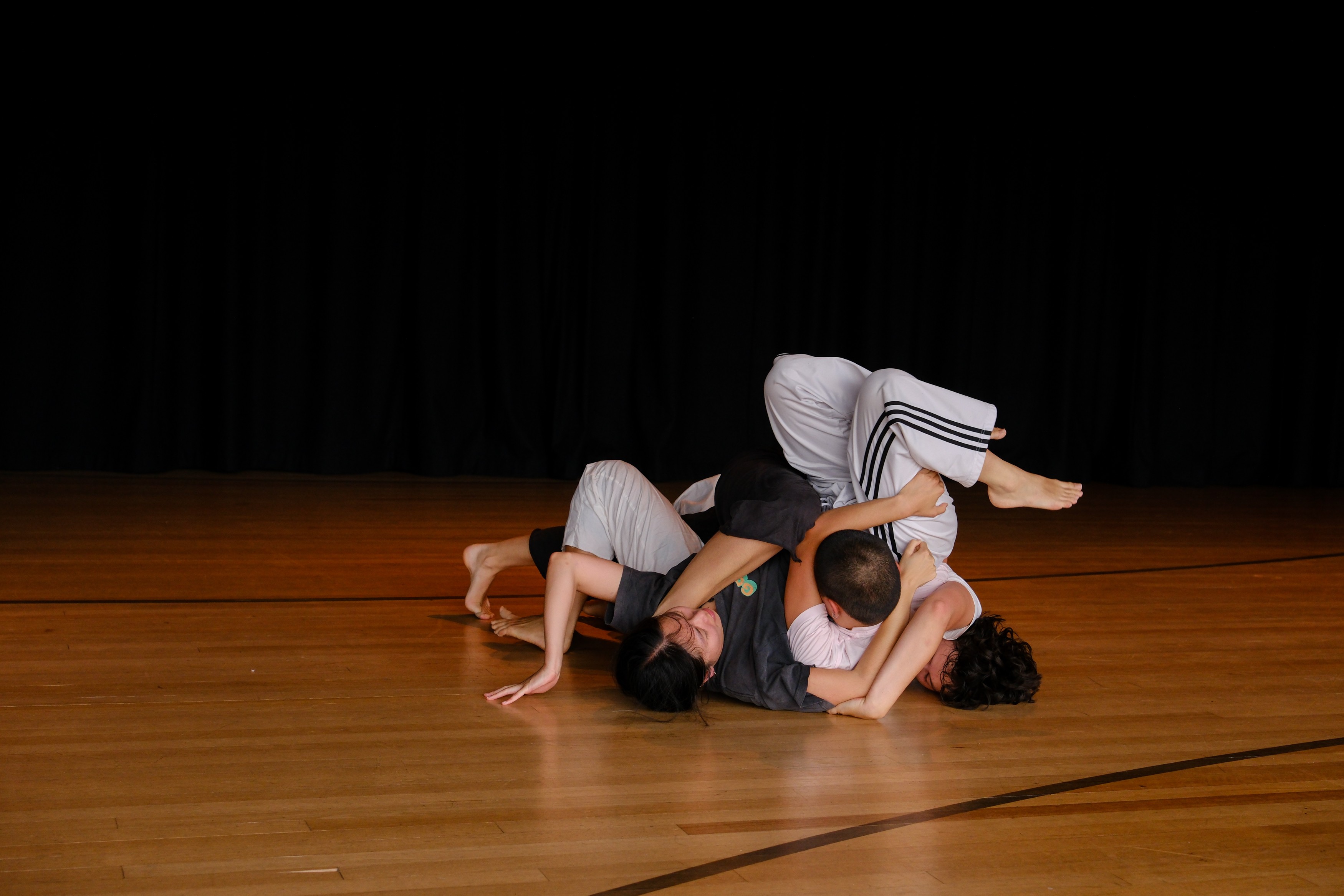 Three young dancers entangled in a knot on a wooden floor