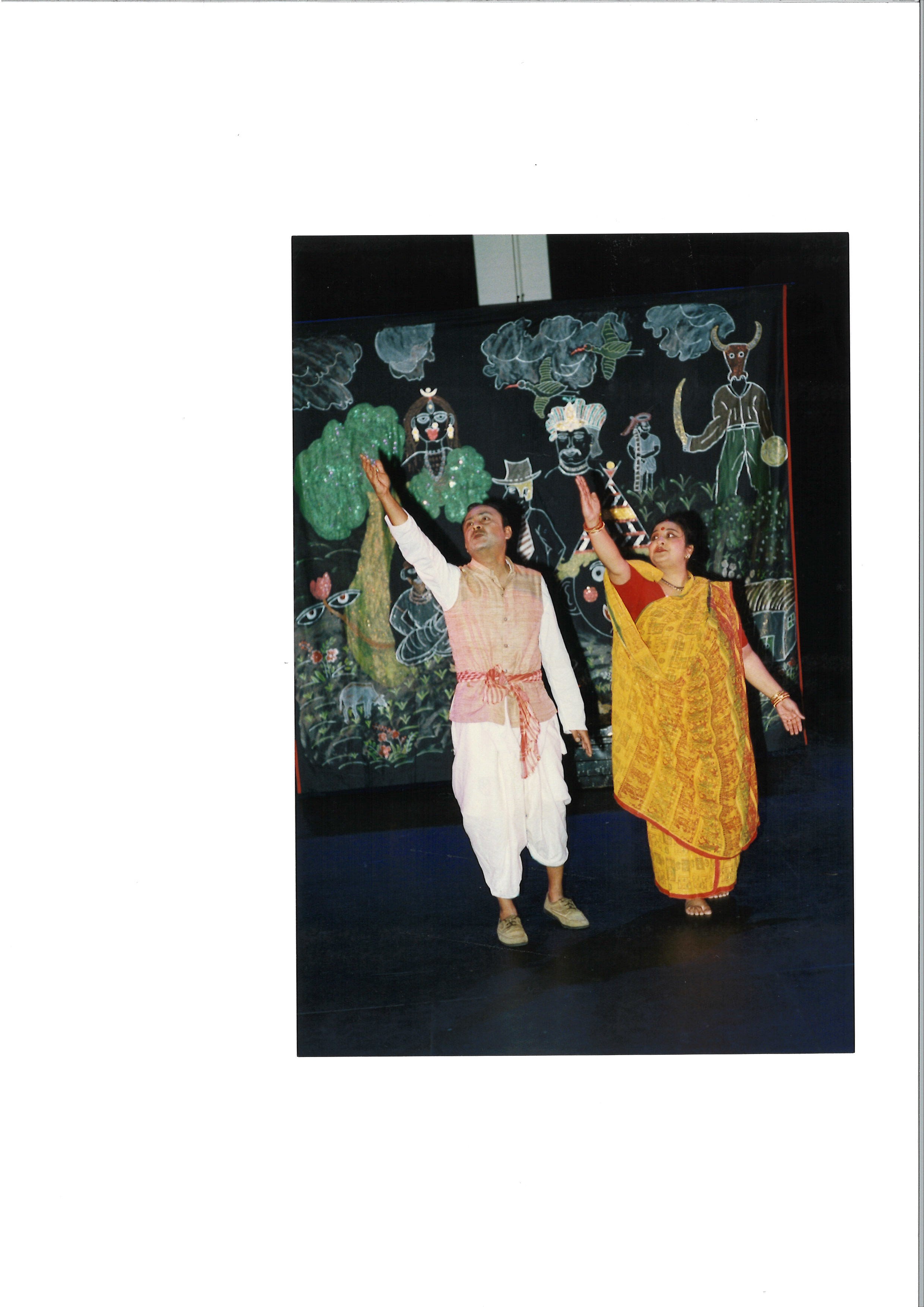 A man and woman with their right arms outstretched, dancing in front of a beautifully embroidered backdrop