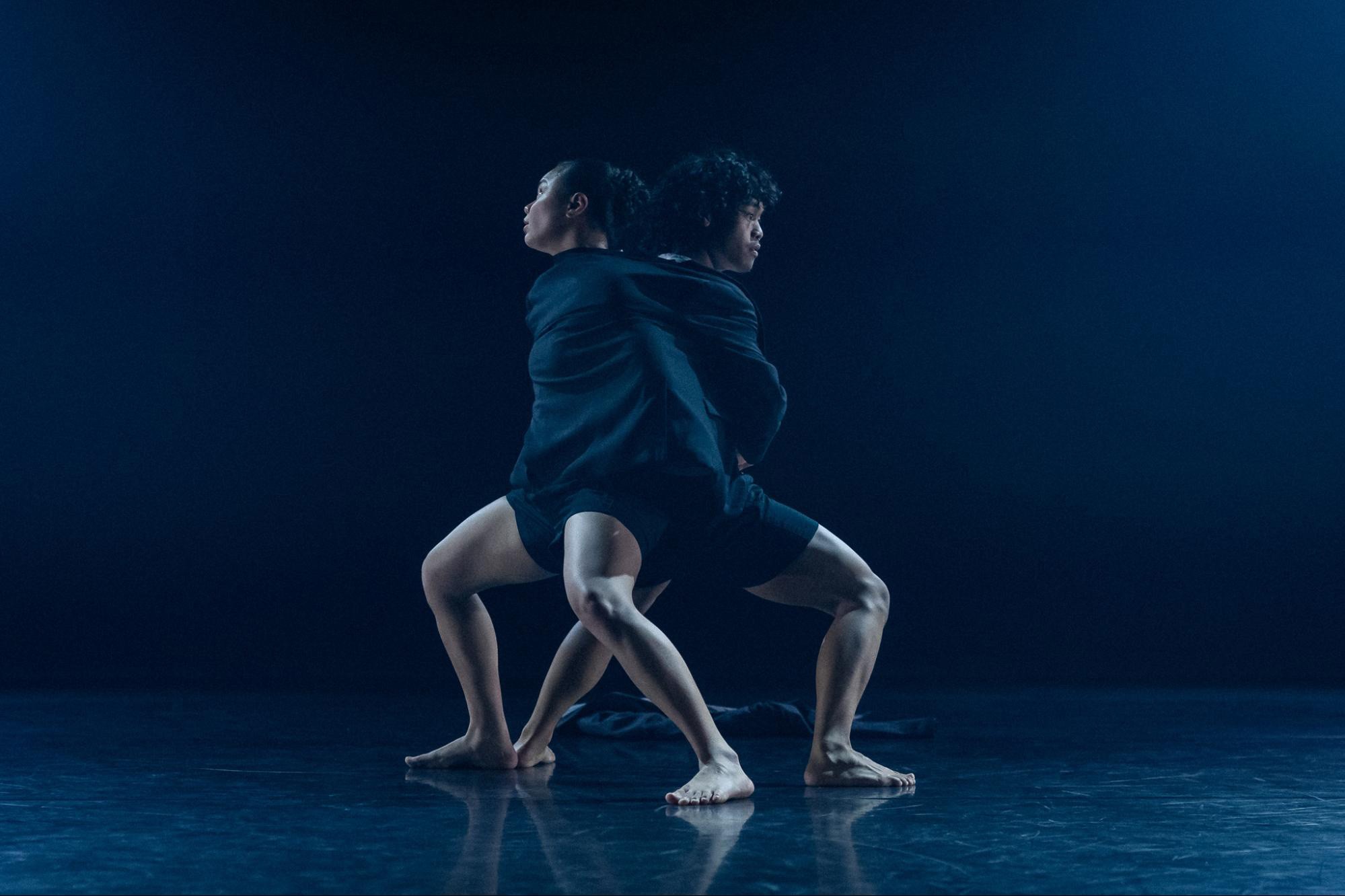 Action photo of a dance performance with 2 people dancing back-to-back wearing a costume that binds them together