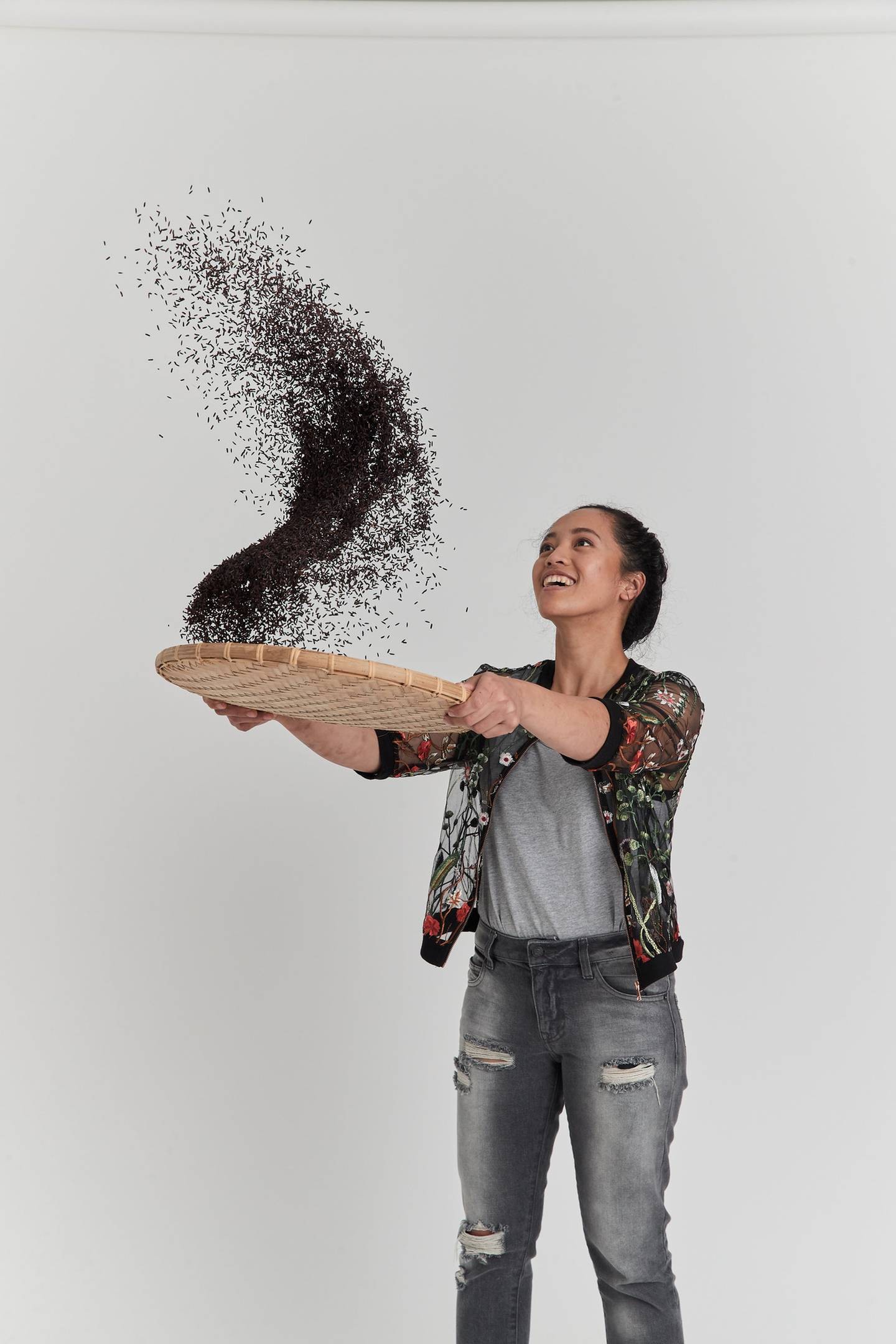 A smiling person of FIlipino descent winnowing black grains of rice using a brown shallow basket