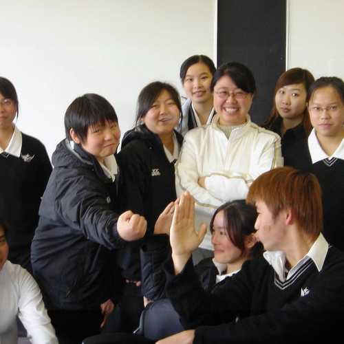 In a classroom, nine students in uniforms pose in a group with their teacher, standing in the centre.
