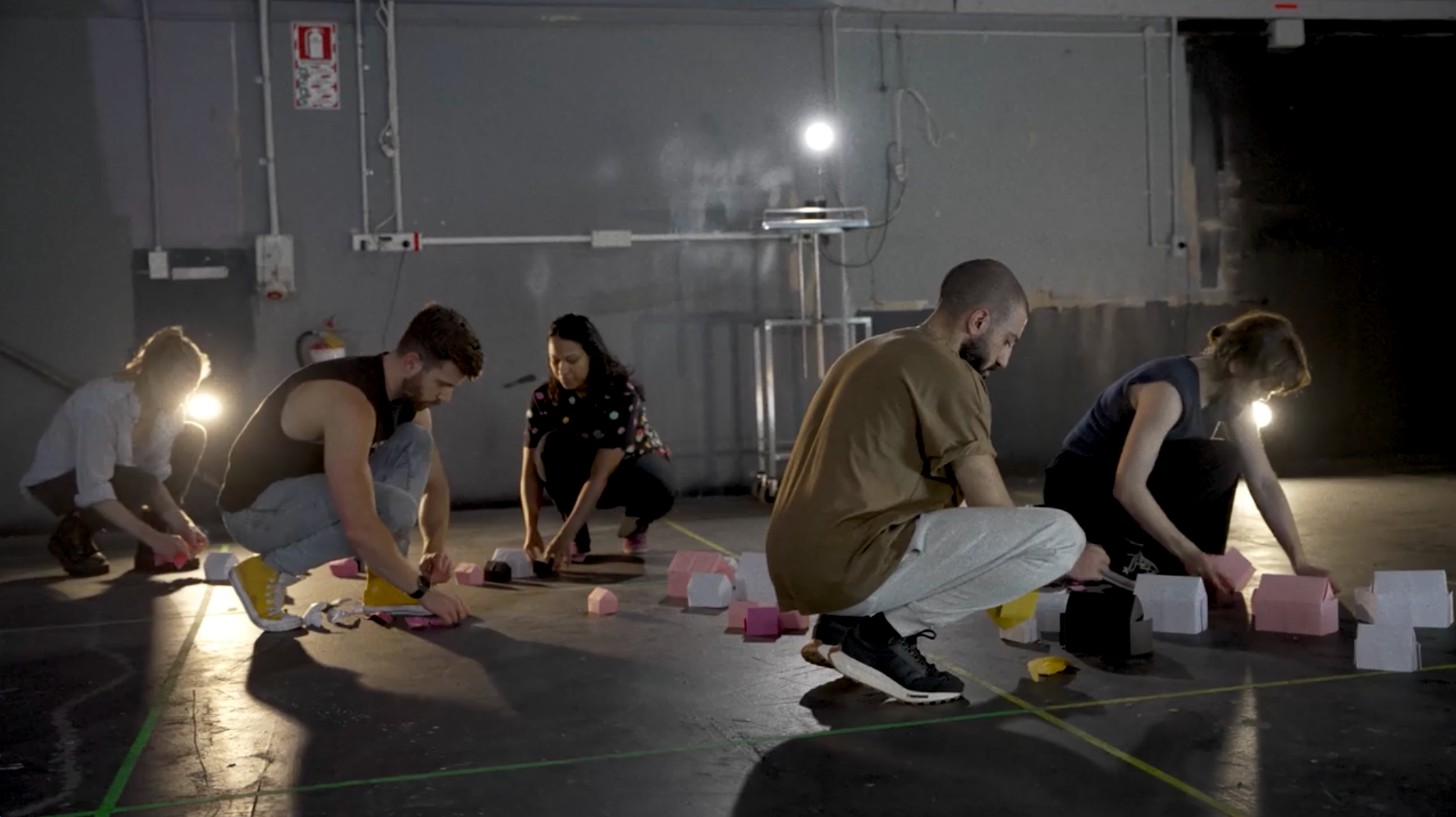 A group of people in a rehearsal space kneeling down on the ground