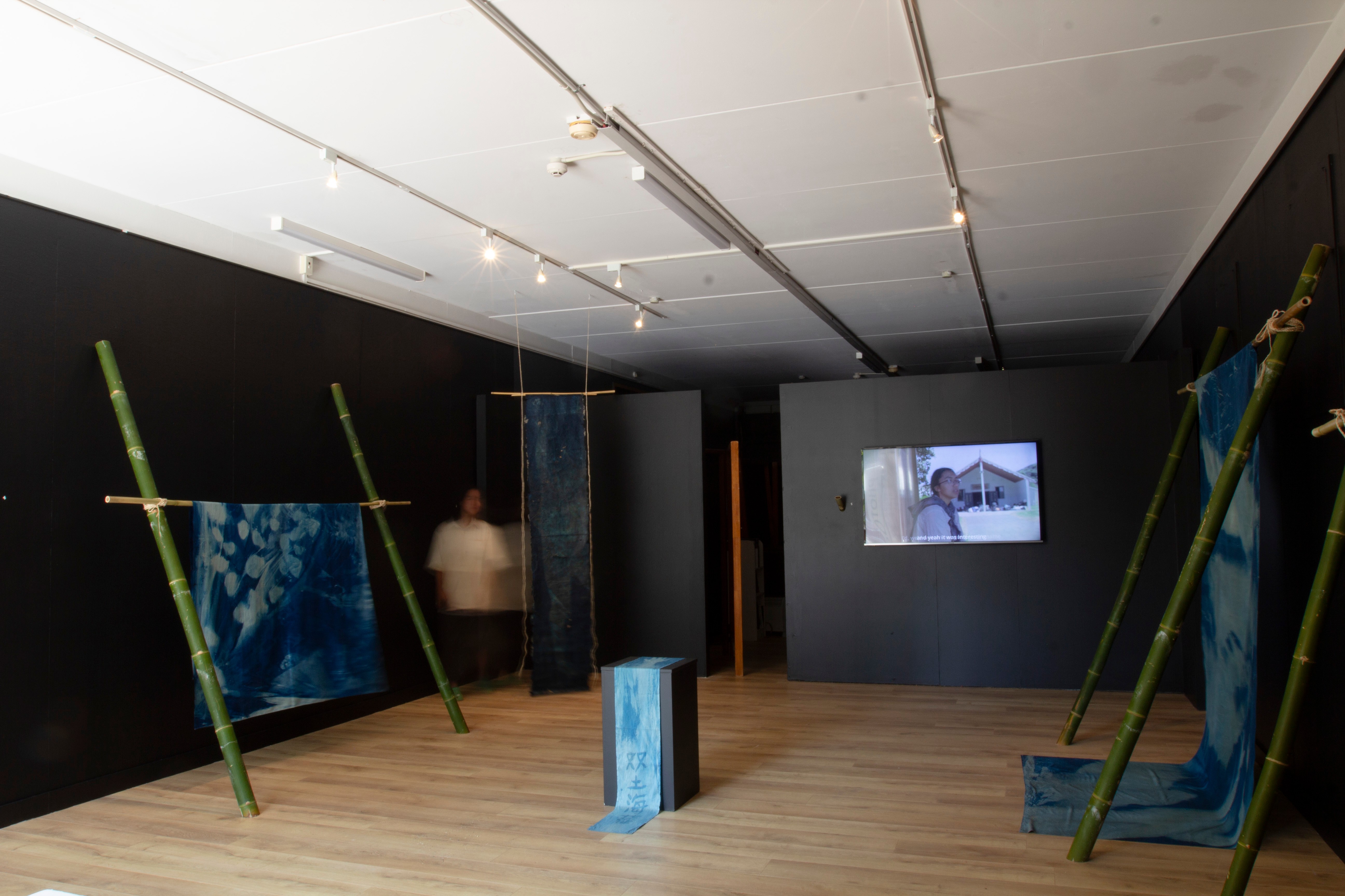 A room with black walls featuring textile works and a film