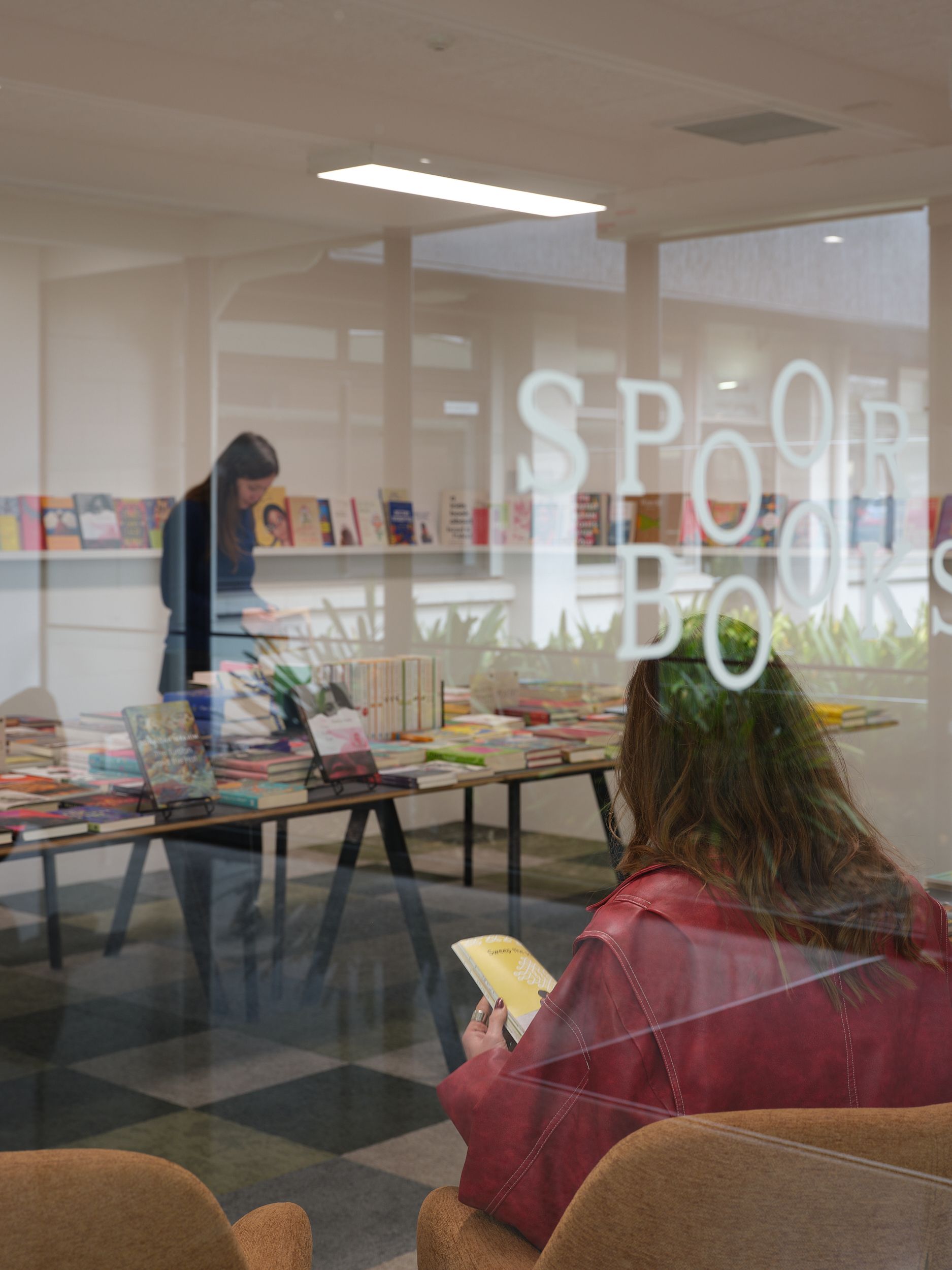 A room featuring a table of books and two people browsing