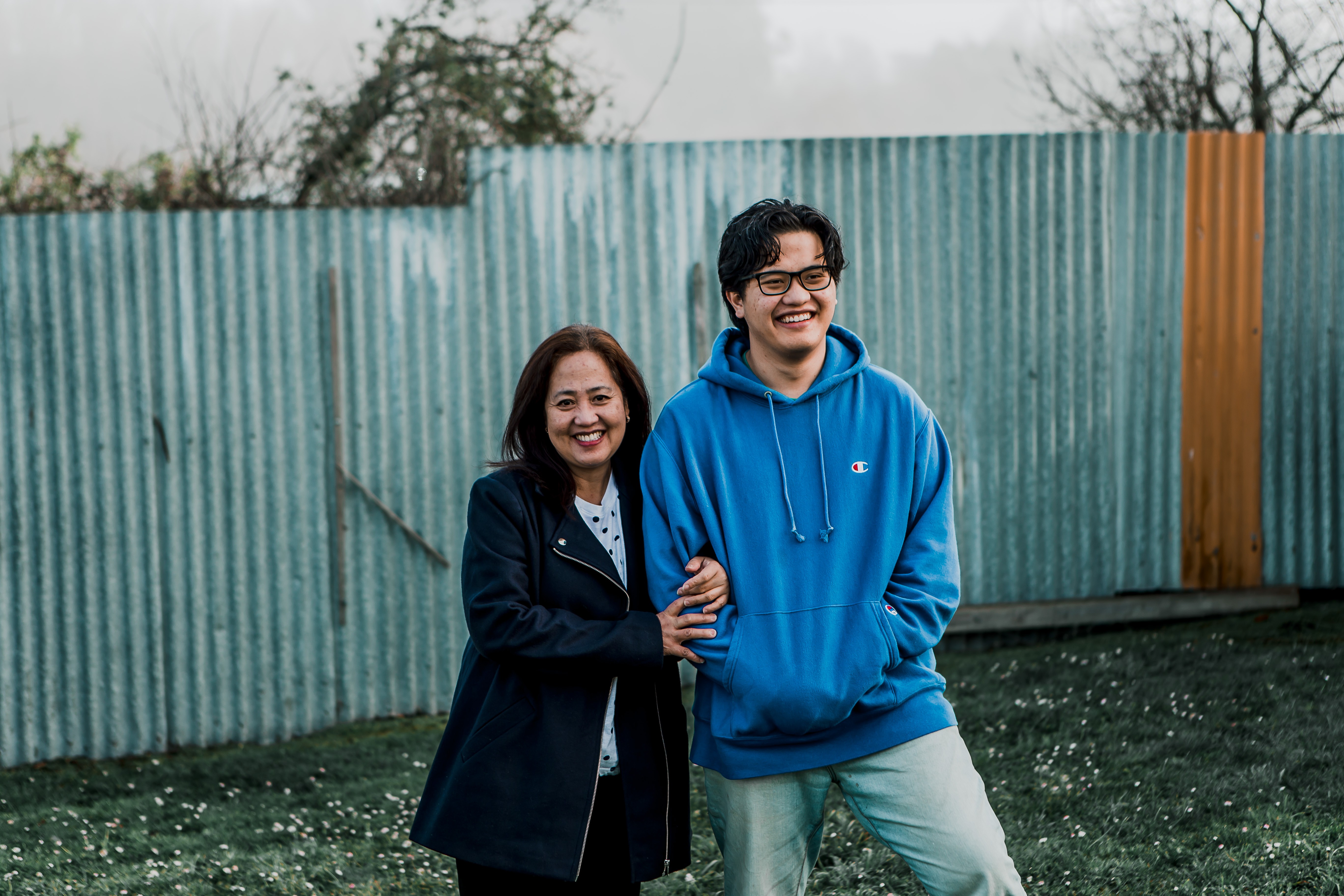 A mother and son arm in arm, smiling and laughing in a backyard.