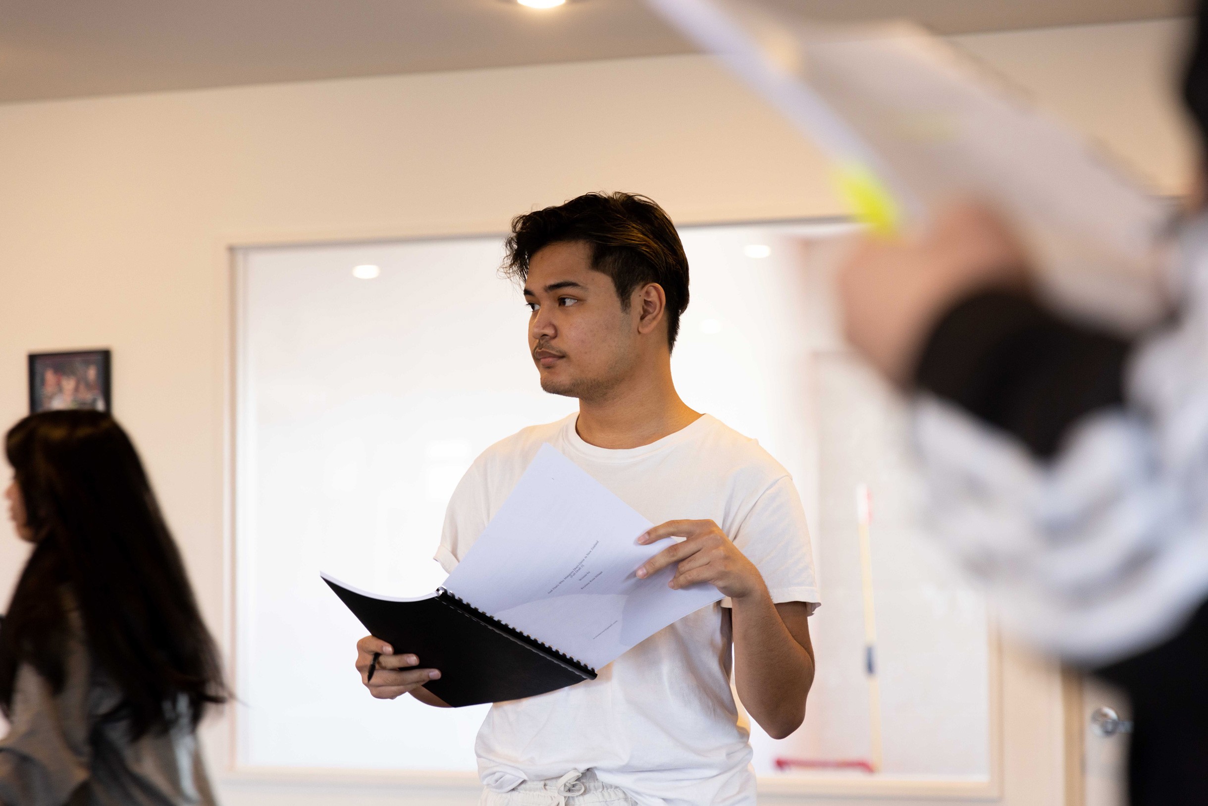 Filipino-looking person  wearing white shirt holding ring-bound script