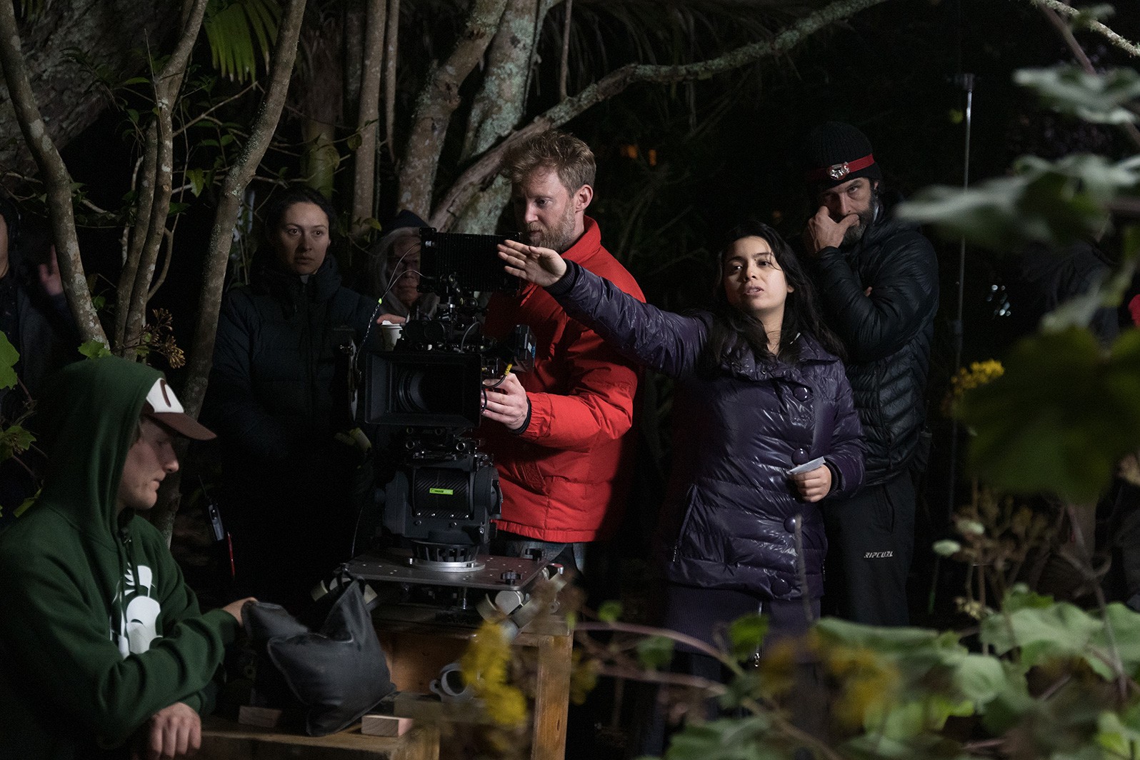 A Filipina in a black puffer jacket directing a scene with her crew behind her