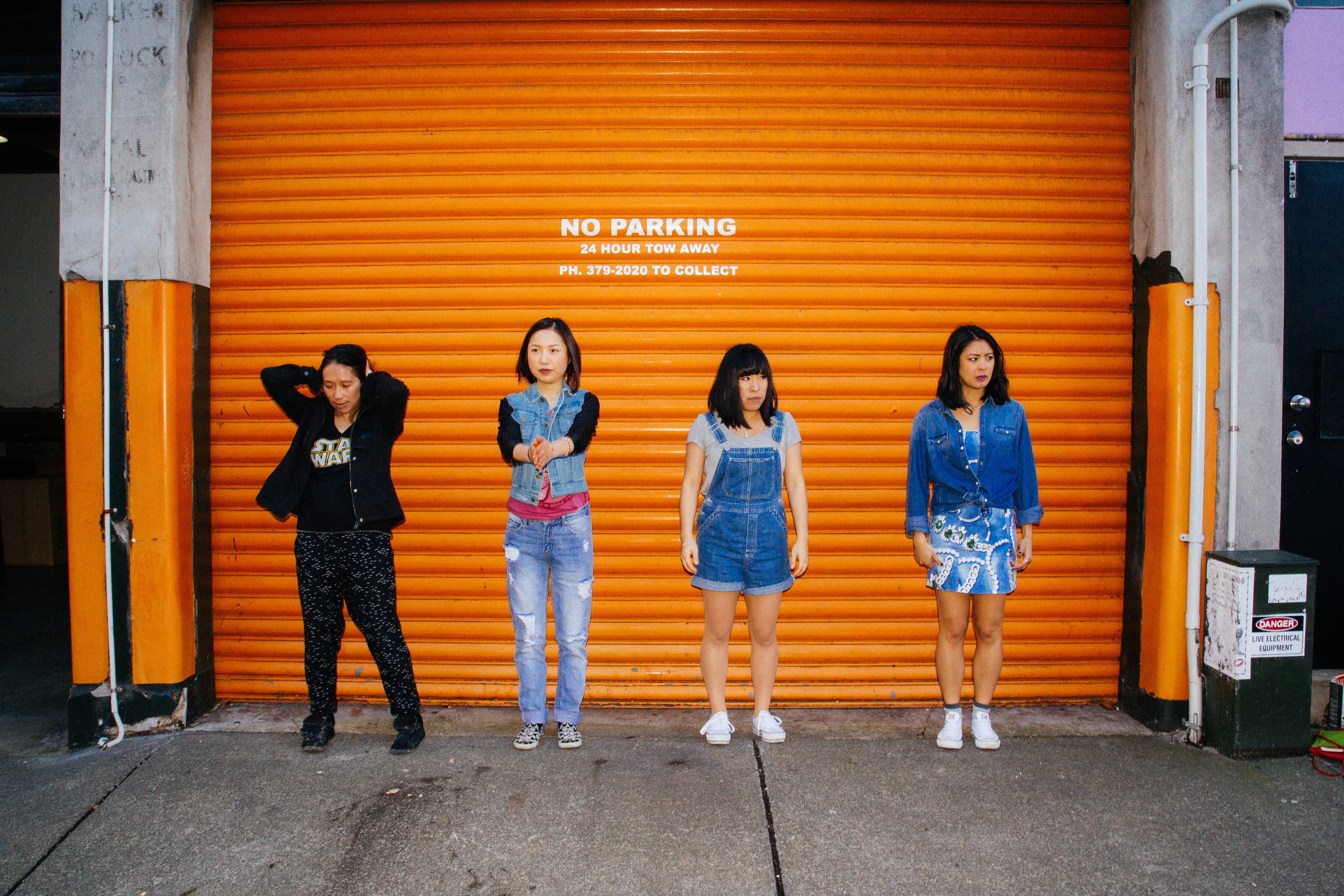 Three East Asian women stand in front of orange garage door