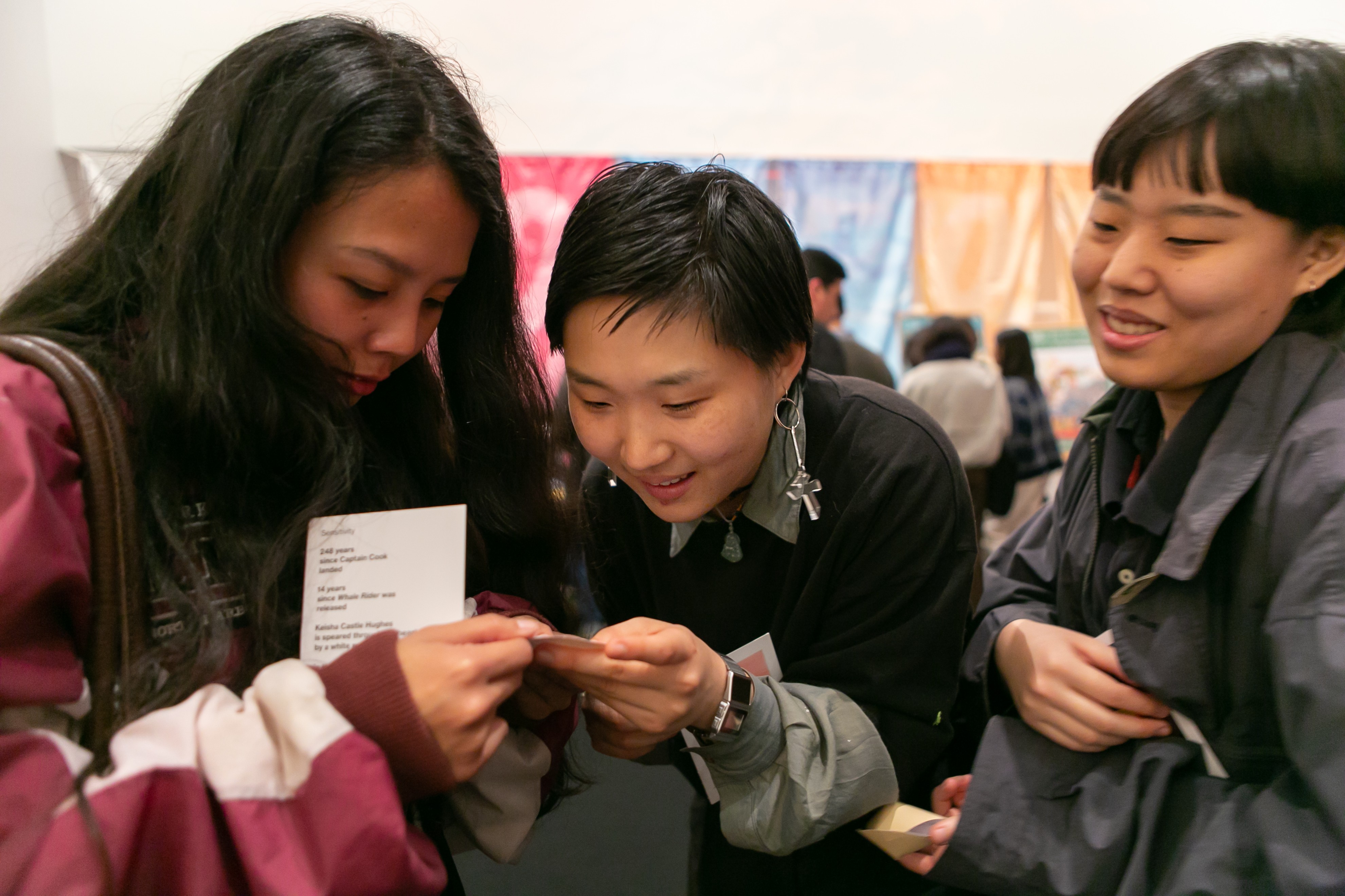 Three young people huddle around a piece of paper in a busy museum