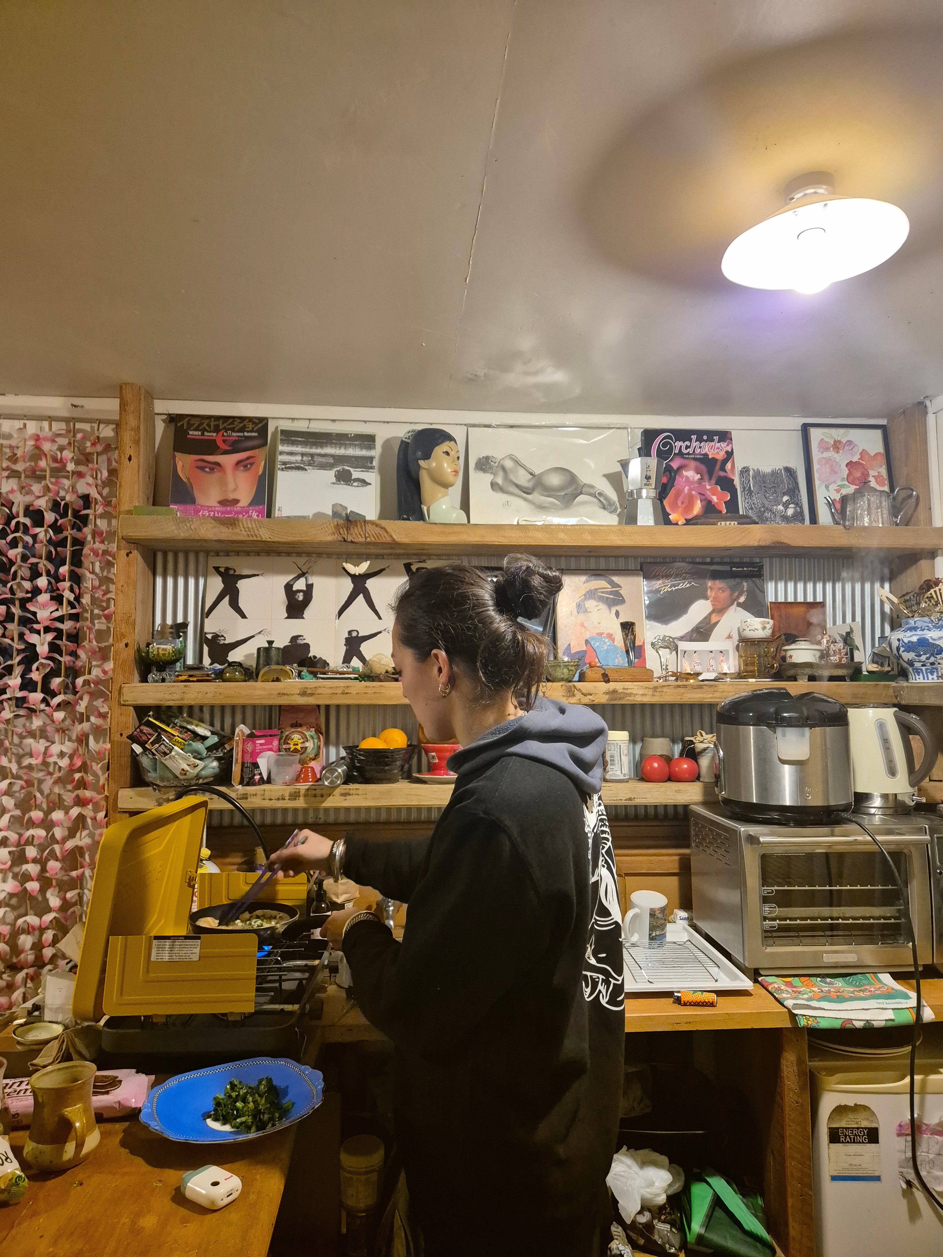 Woman with black hair tied in a bun faces away from camera, focused on what she is cooking