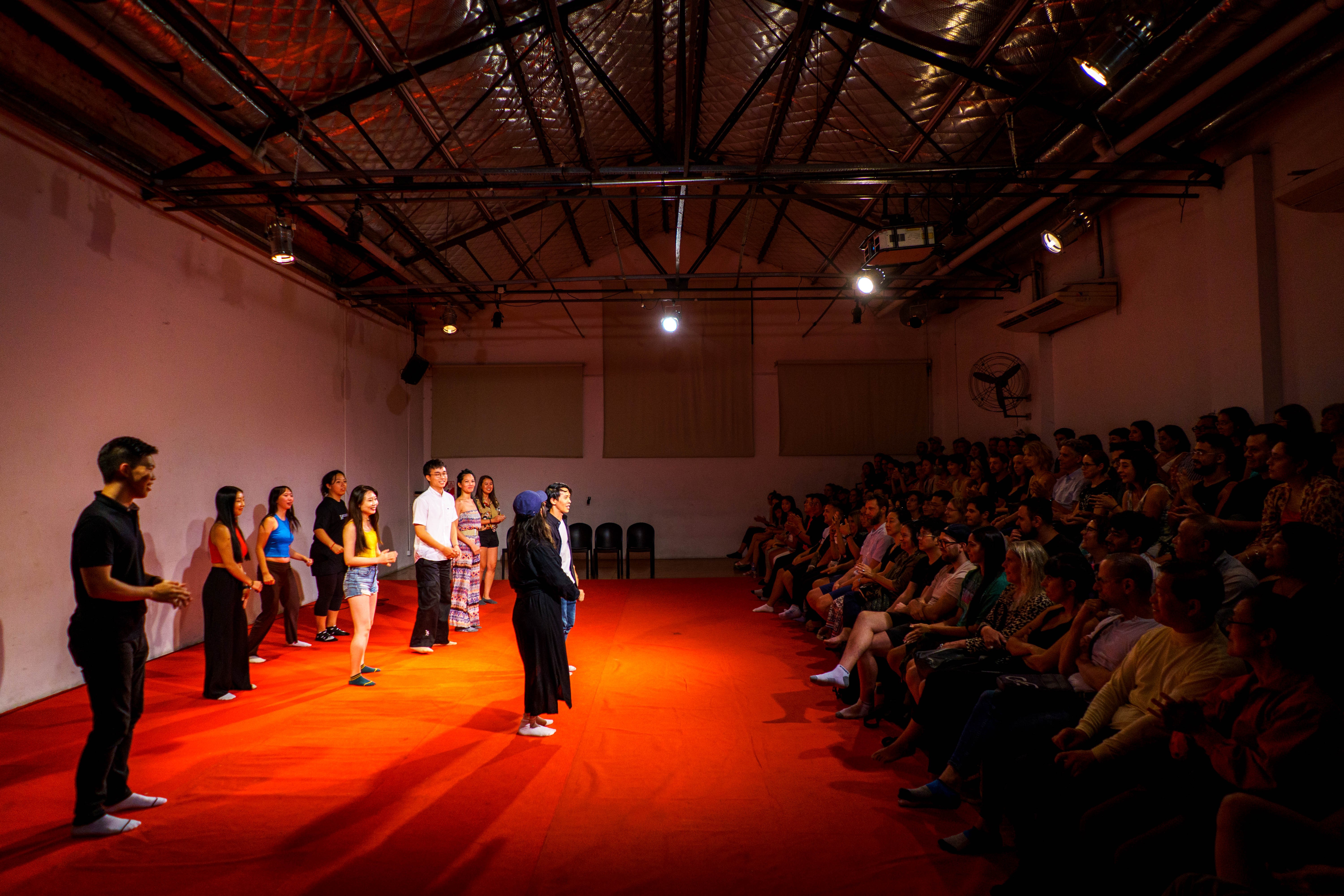 A group of people standing in. aline on a red carpet looking at the audience