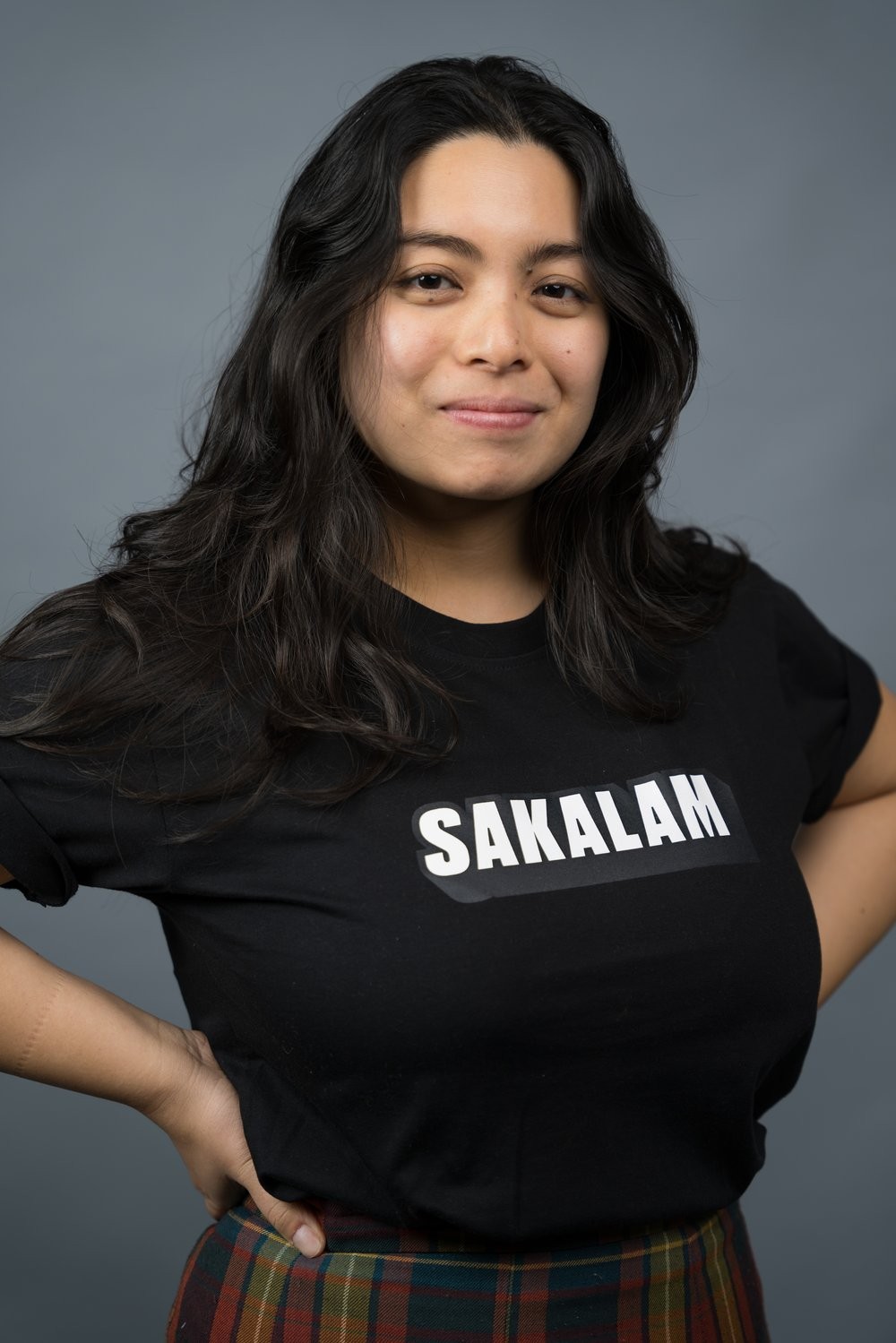 A Filipina with long hair smiling with hands on hips, wearing a black shirt with white text that says 'SAKALAM'