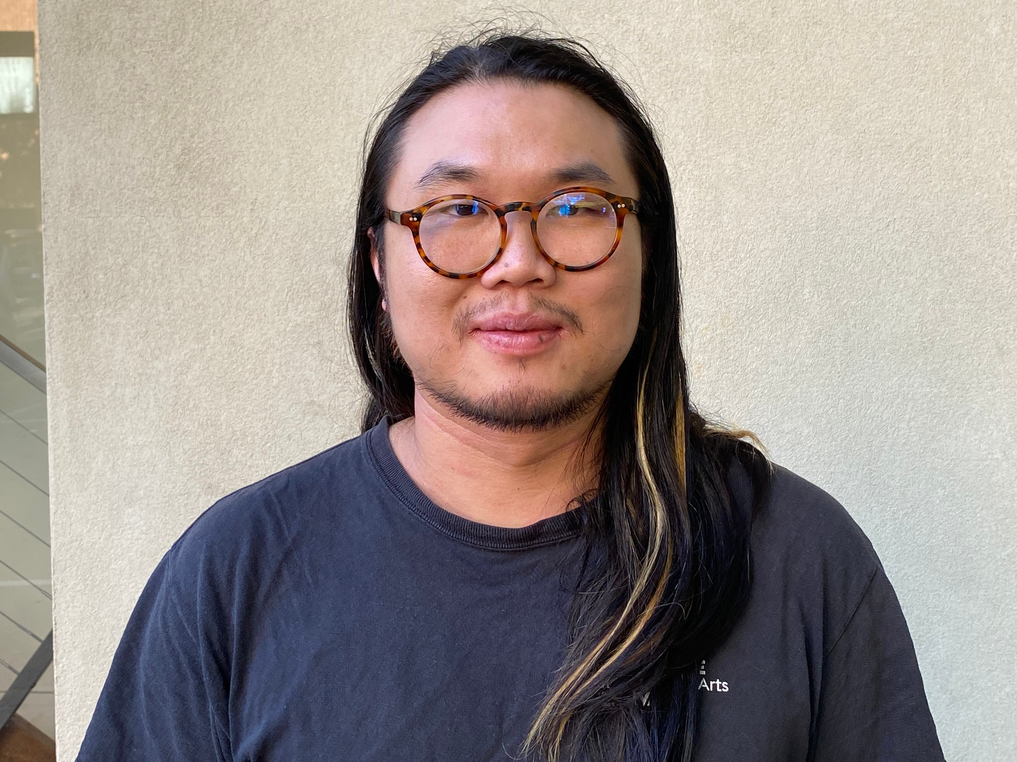 Head and shoulders portrait of a long haired man with facial hair wearing glasses 