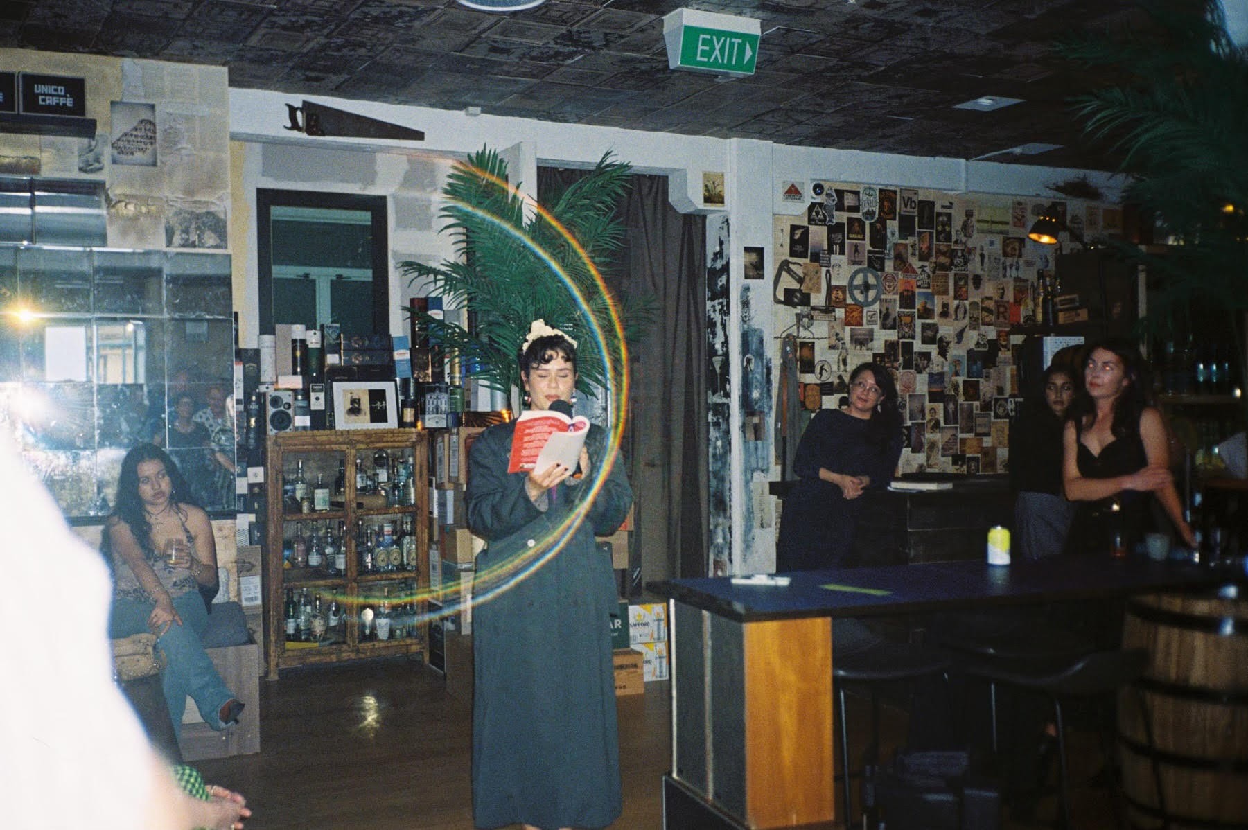 A film photo of a woman reading from a book in a bar