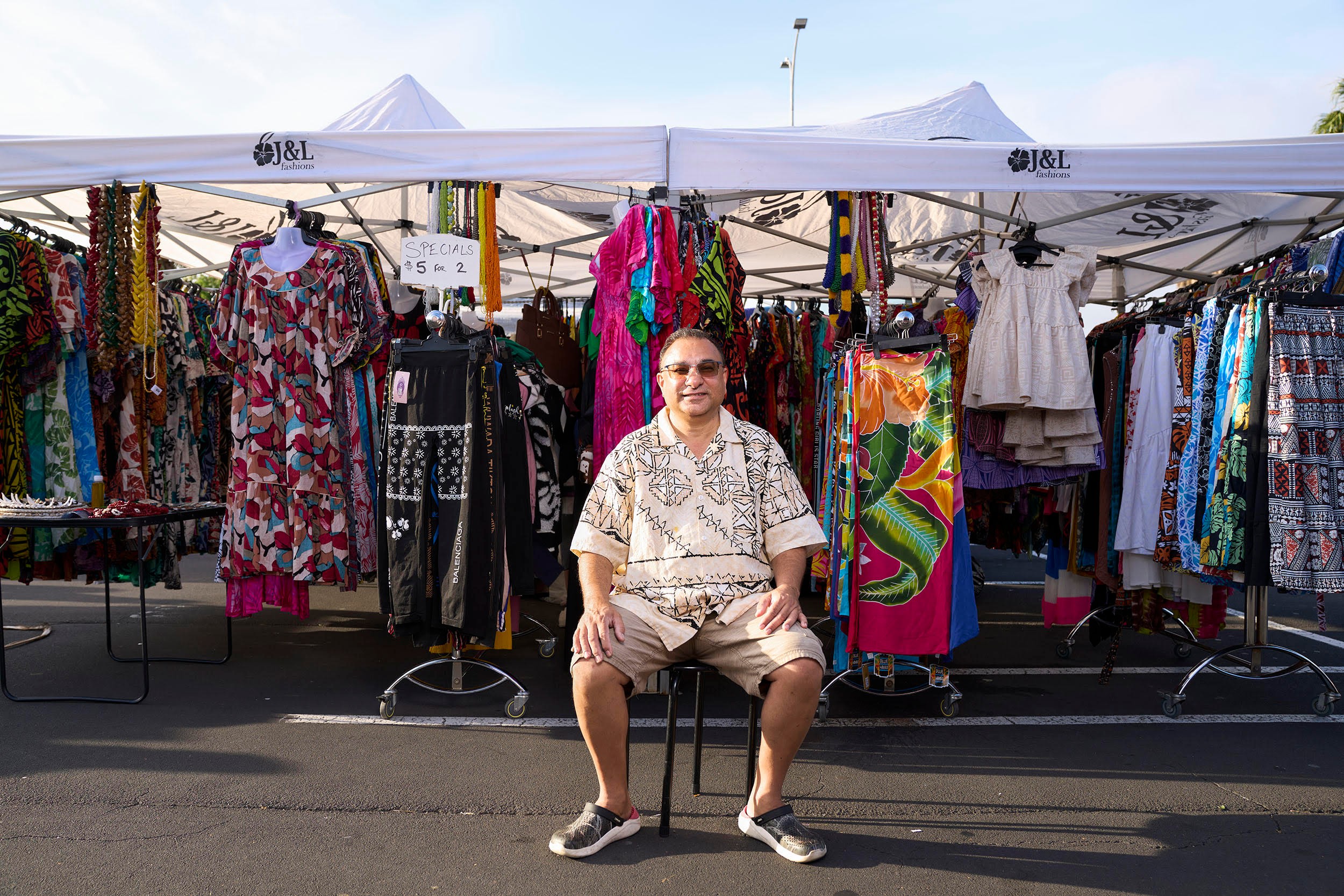 A man sits in front of his outdoor stall selling clothes