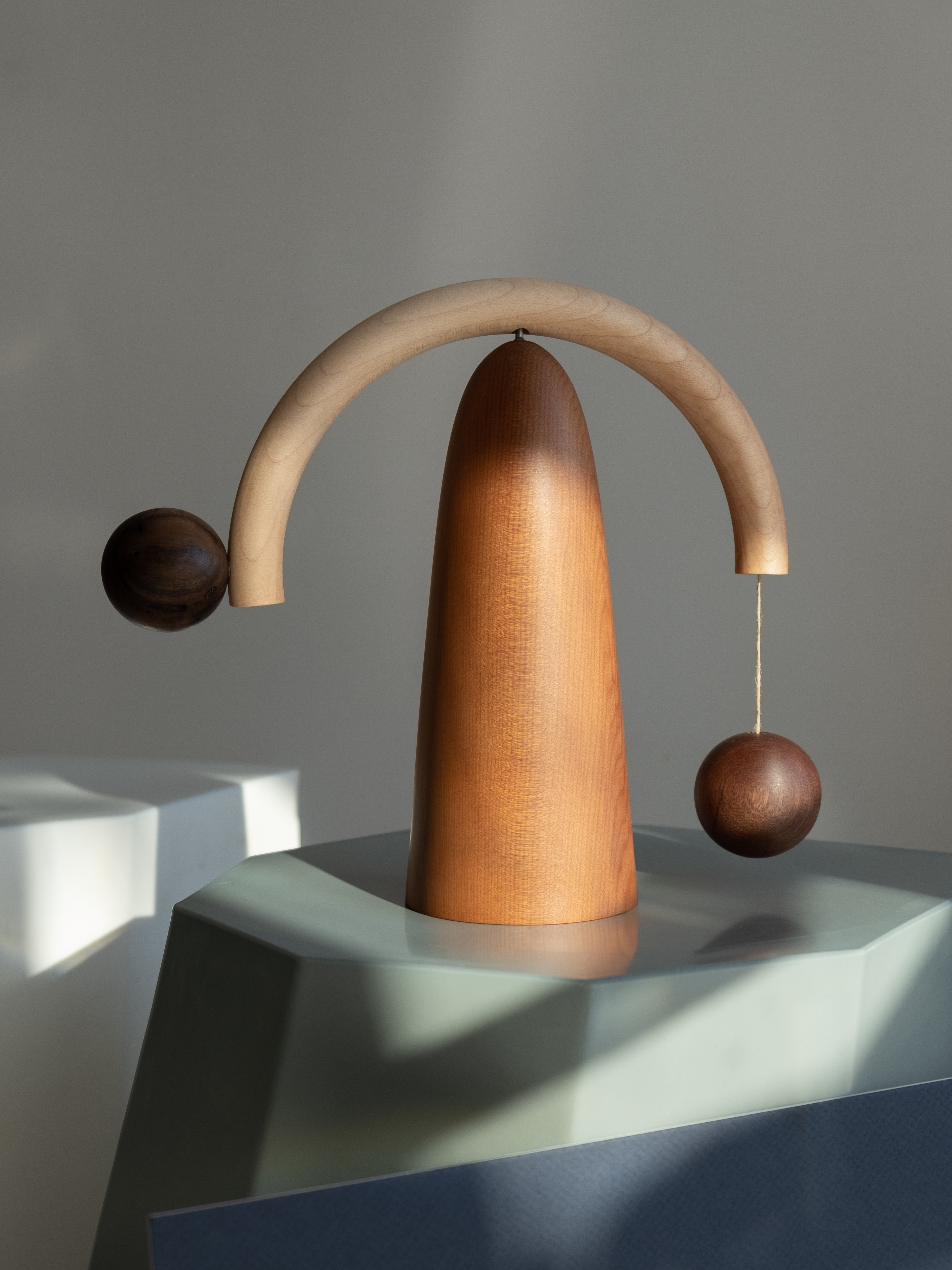 A finger shaped wooden stand. Balanced on top is a thin half-circle rod with two round balls hanging from them like a mobile