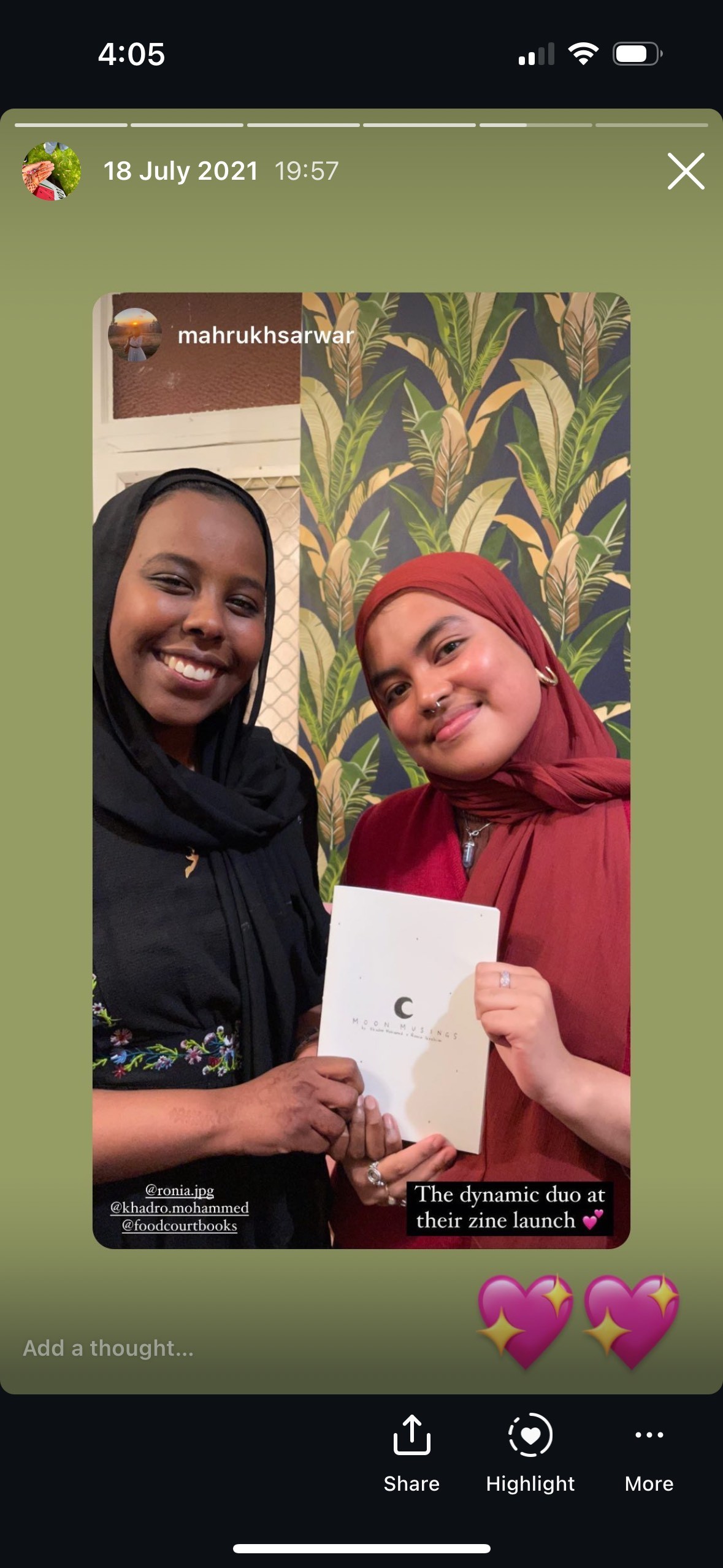 Two people smiling and holding a zine. There are two heart emojis on the image. 