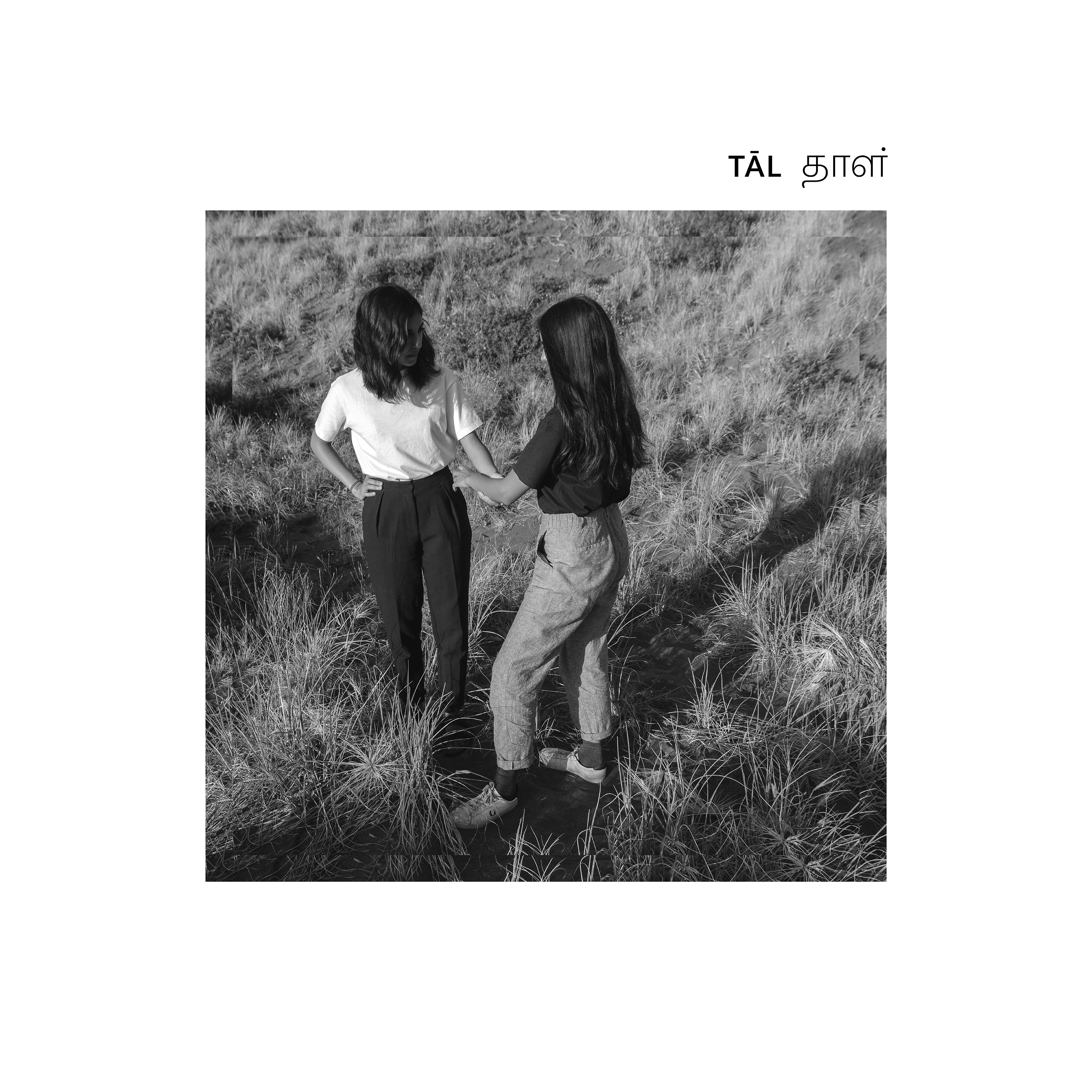 A square balck and white photograph of two people standing together in a field