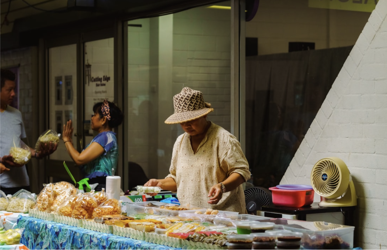 A woman in a woven hat stands at a colourful market stall.