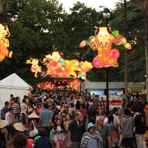Illuminated Chinese lanterns hang above a crowd of people surrounded by trees