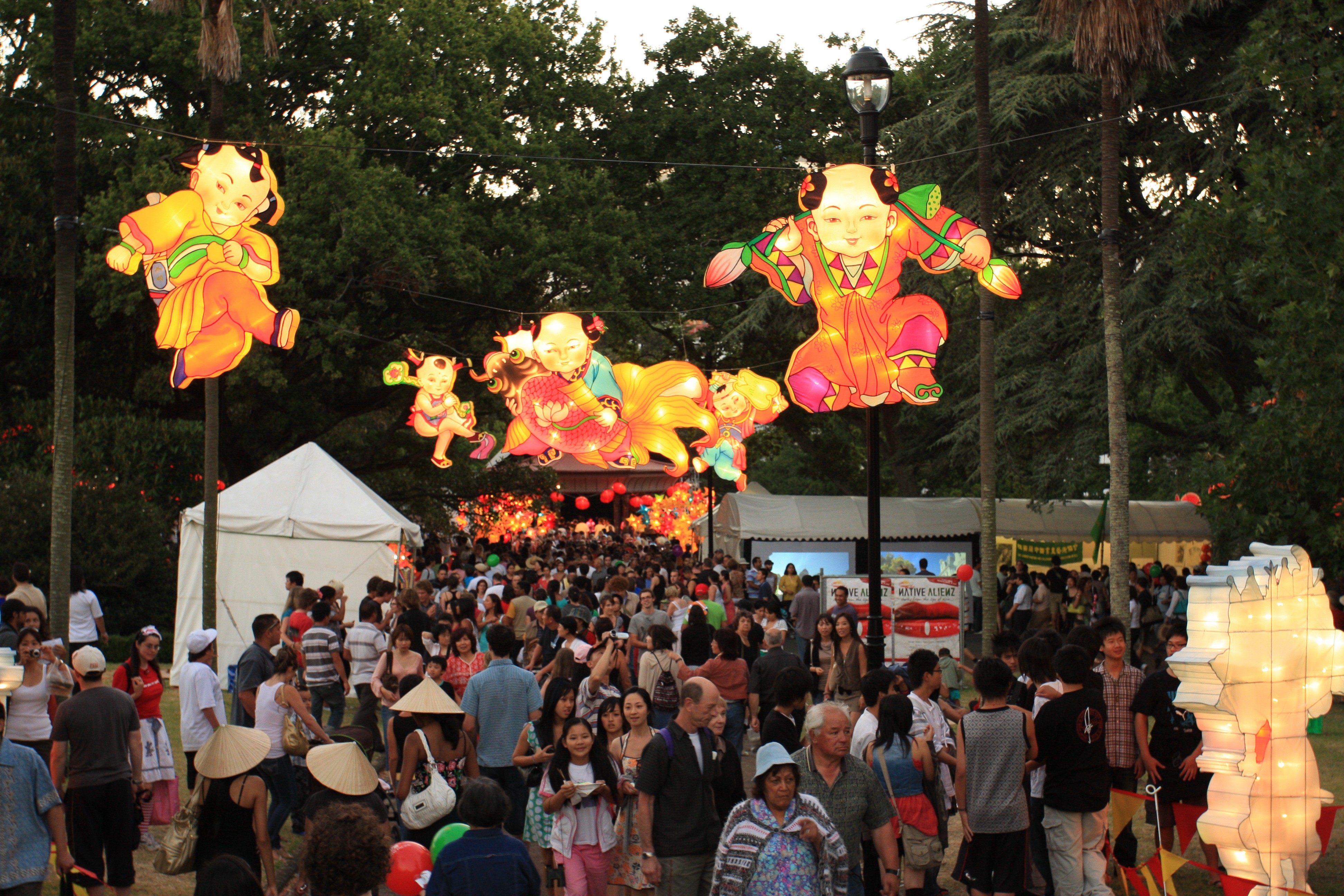 Illuminated Chinese lanterns hang above a crowd of people surrounded by trees