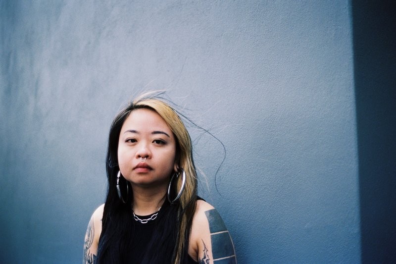 A woman with large hoop earings and long black hair with a bleached streak looks at the camera