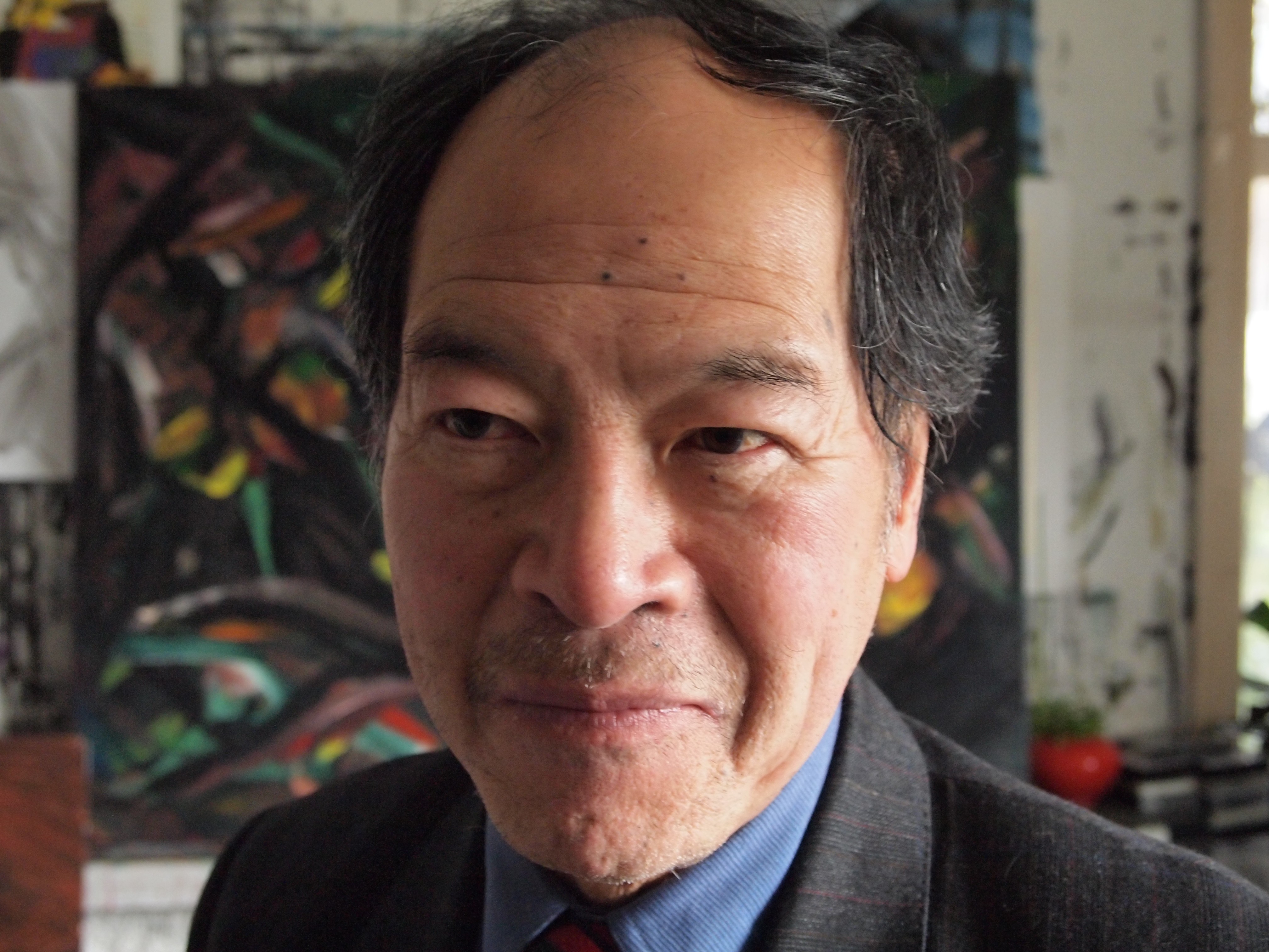 Close-up of a man standing in an artist studio with a painting behind him.