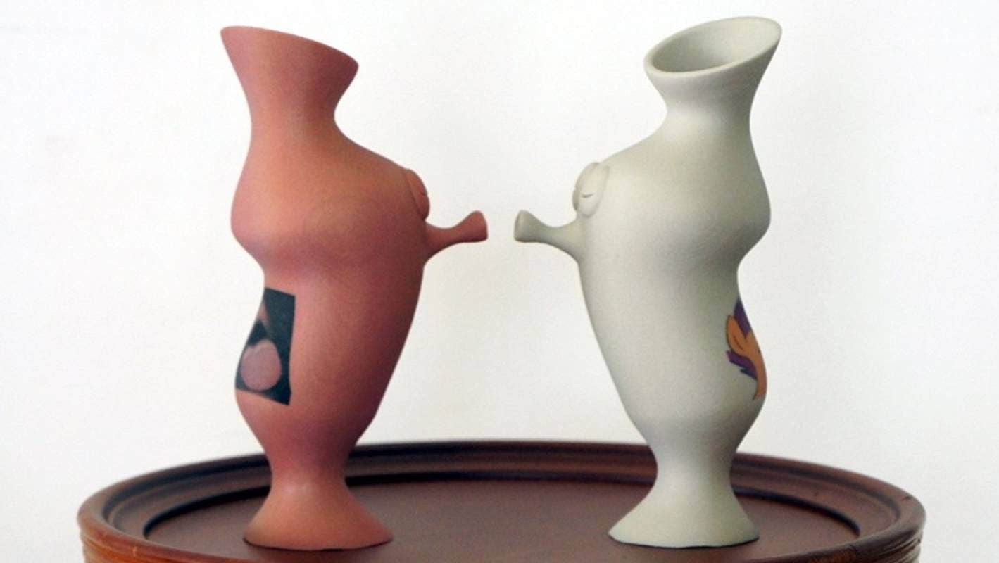 Two anthropomorphic vases lean towards each other, eyes closed and lips puckered for a kiss.