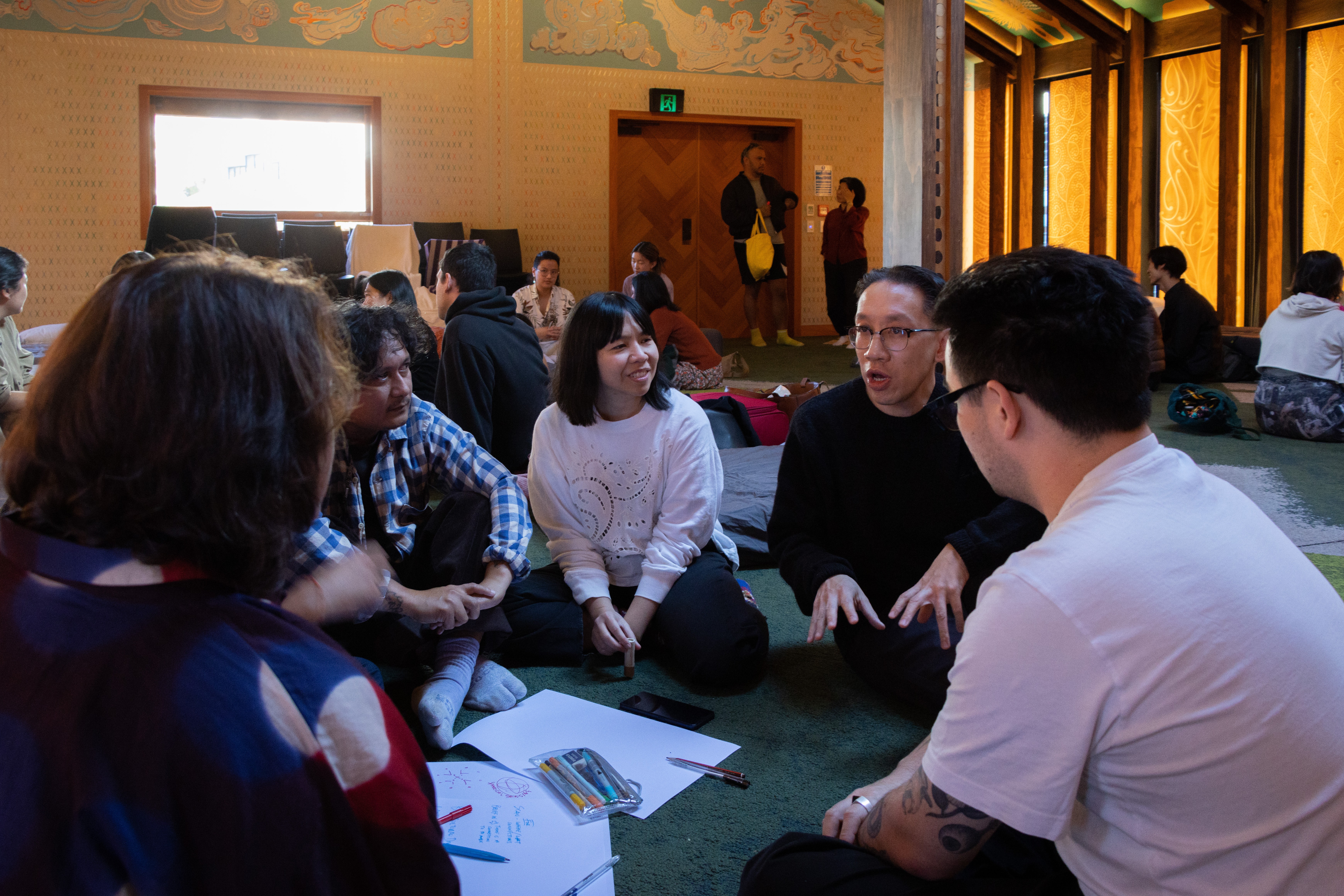 A group of people sitting cross-legged in a marae having a discussion