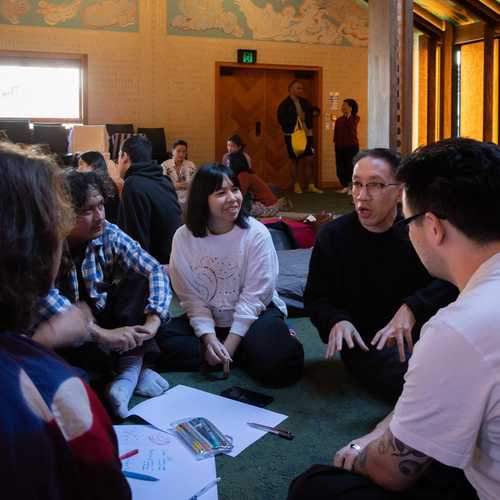A group of people sitting cross-legged in a marae having a discussion