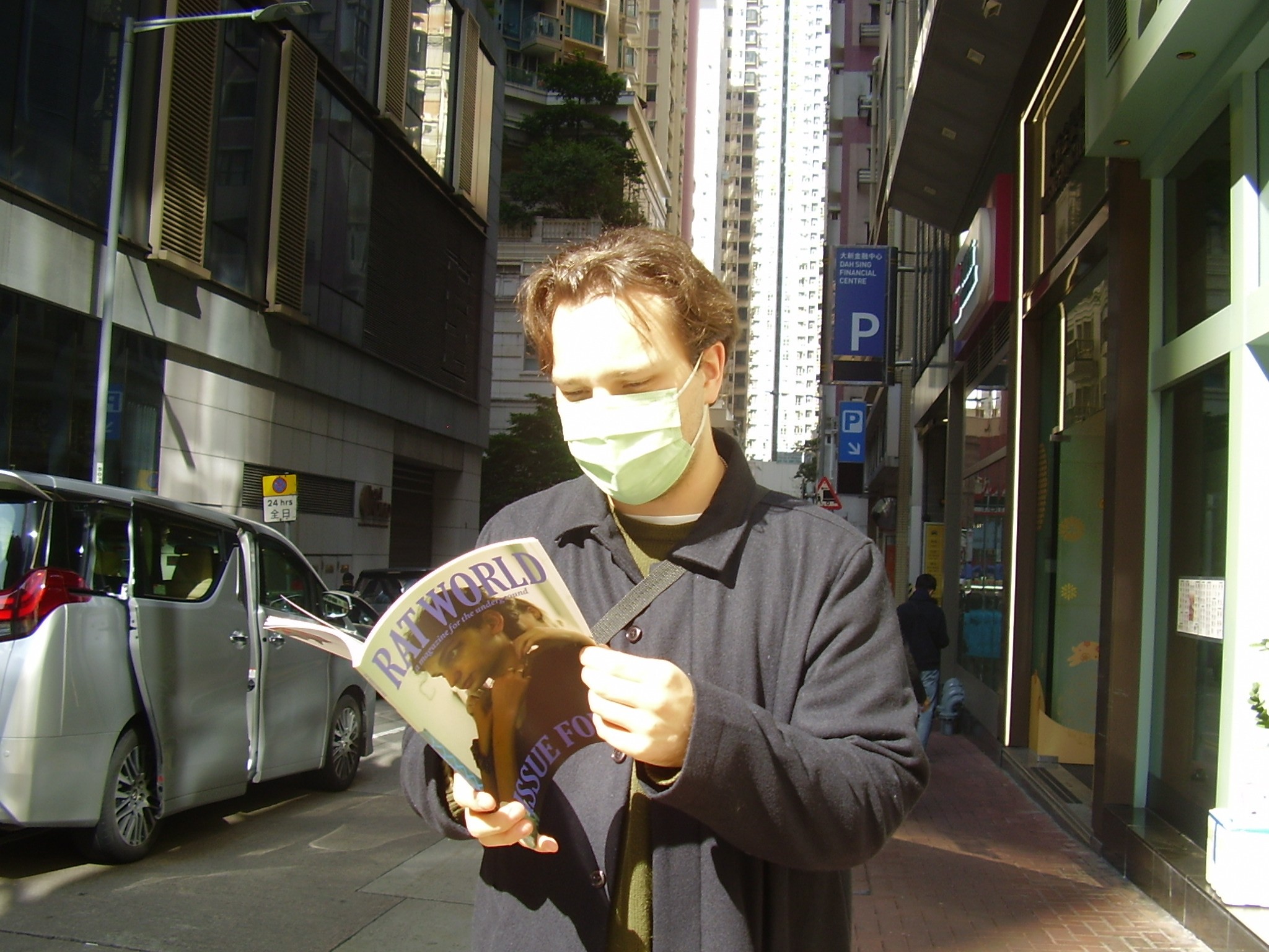 Aidan wearing a mask and reading Rat World on a city street.