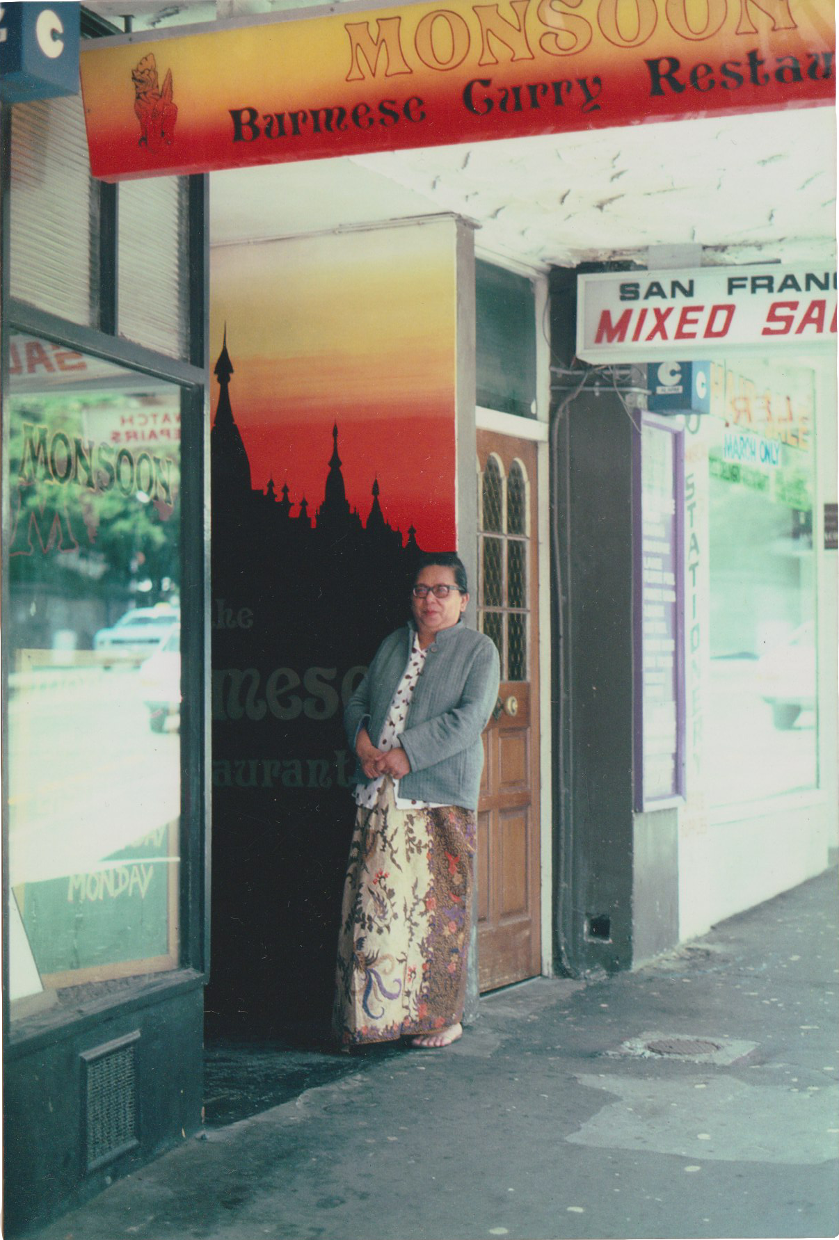 Woman leaning against a doorway under a sign that says 'Monsoon: Burmese Curry Restaurant'.