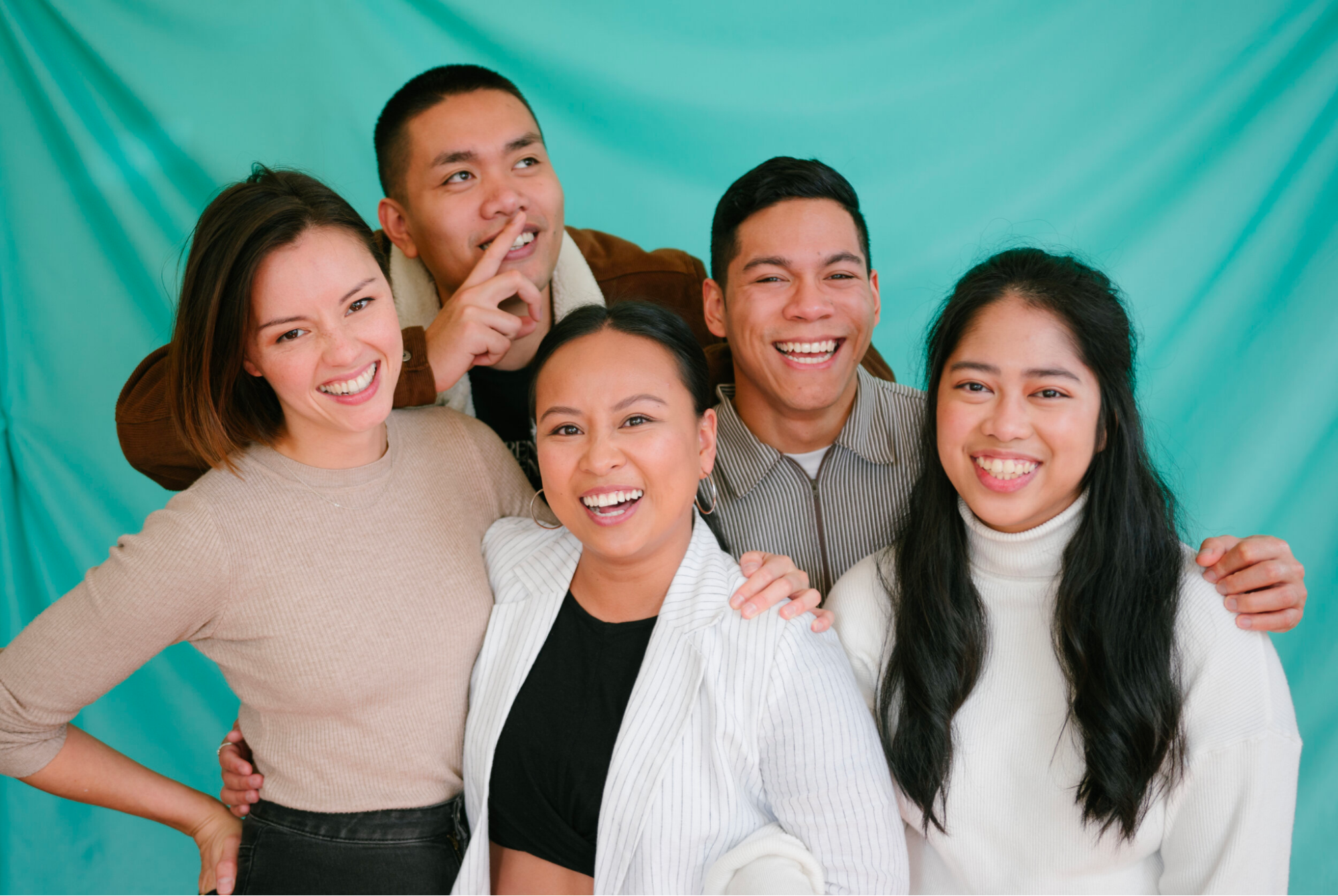 A group of people posing in front of an aquamarine backdrop, all smiling at the camera