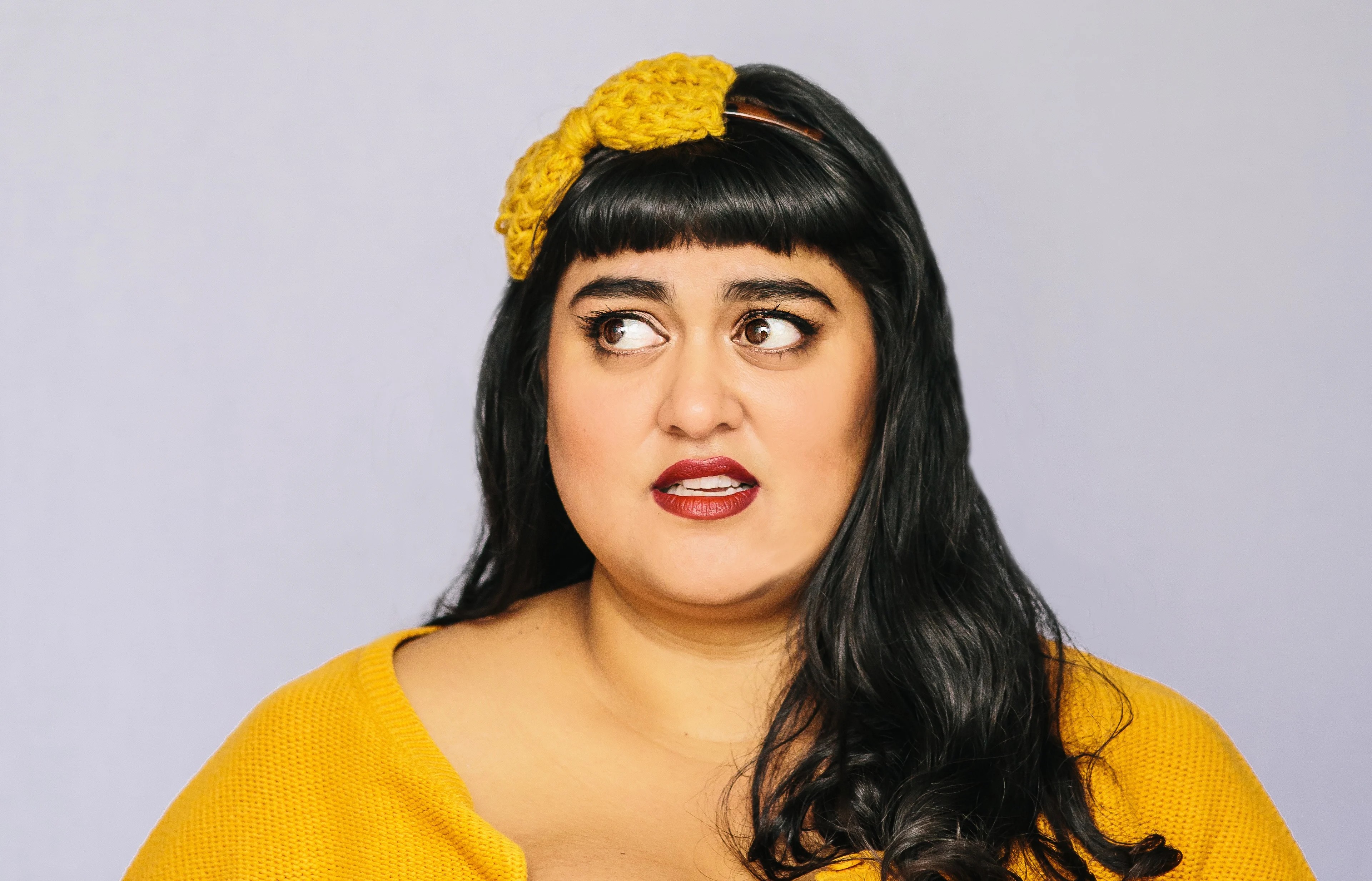 Close-up of a woman with a knitted yellow bow in her black hair and a matching sweater, looking to her right.