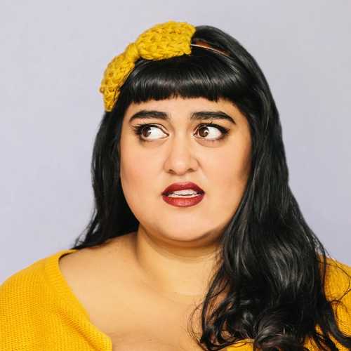 Close-up of a woman with a knitted yellow bow in her black hair and a matching sweater, looking to her right.