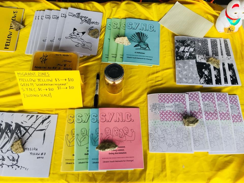 Various colourful zines laid on top of a yellow tablecloth.