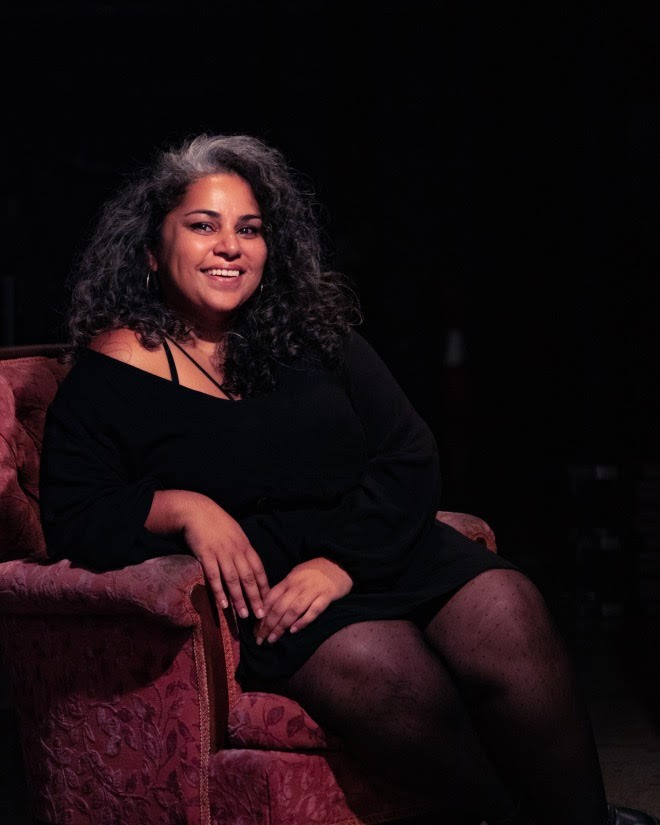 A woman in a black dress sitting on a red velvet armchair, smiling at the camera