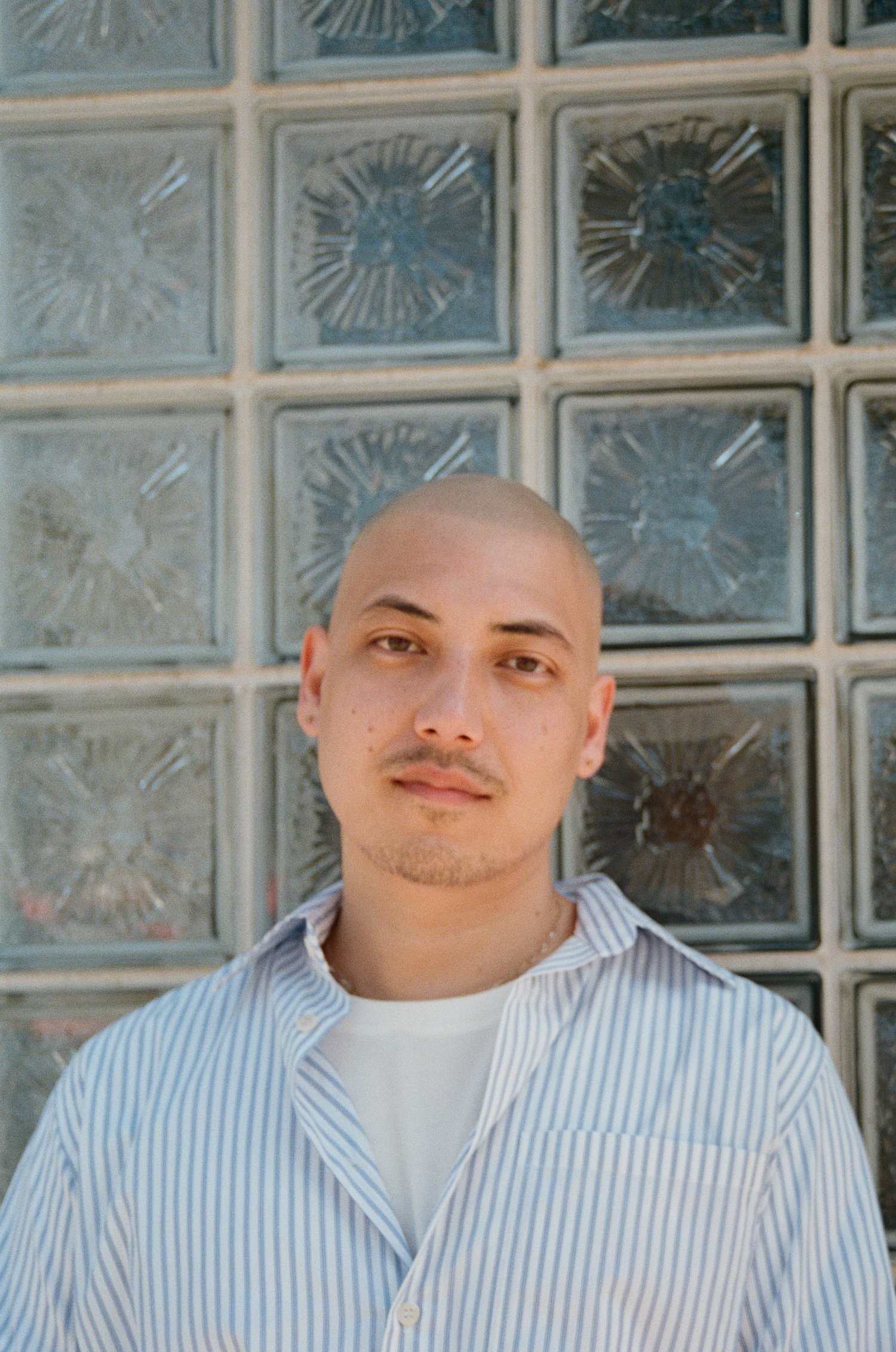 a man with a shaved head and a blue and white striped shirt looking at the camera