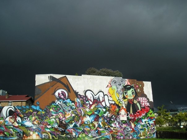 A bright white wall with graffiti on it with dark clouds in the background