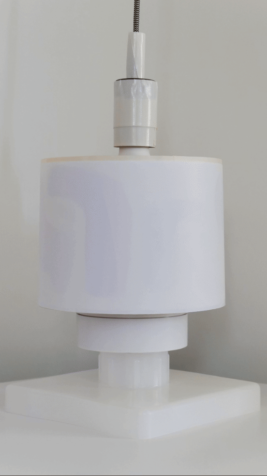 A modern lamp with a vibrant, abstract-patterned lampshade. The shade has colorful, organic shapes in purple, orange, yellow, and blue tones, and is illuminated from within, casting a warm glow.