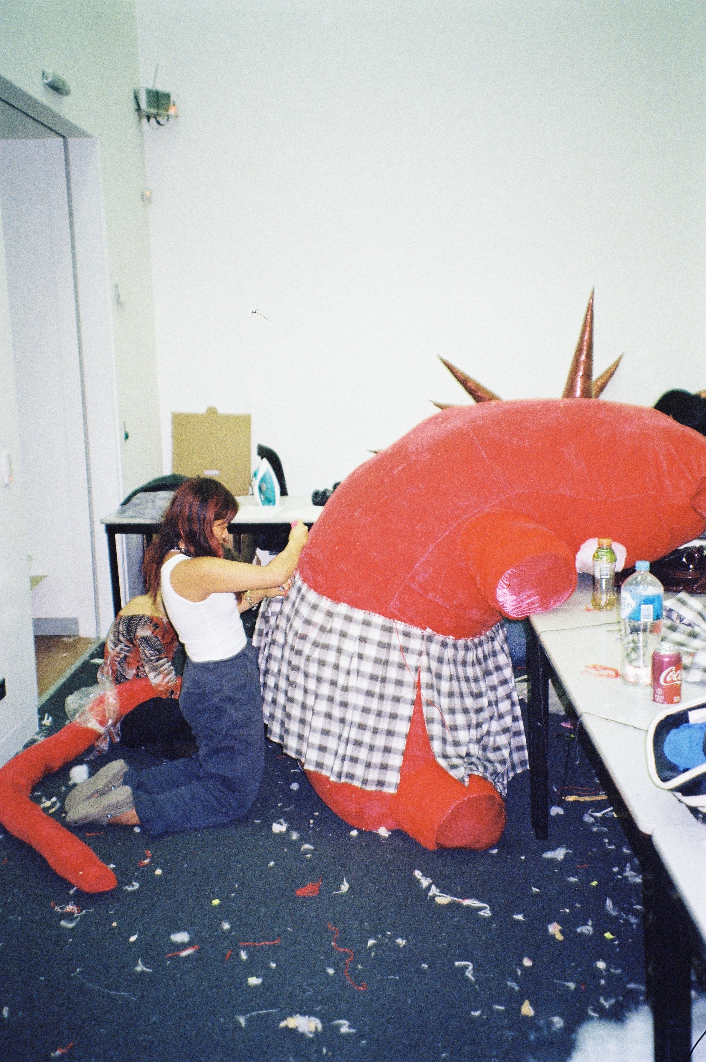 The back of a large red soft toy being sewn by a person