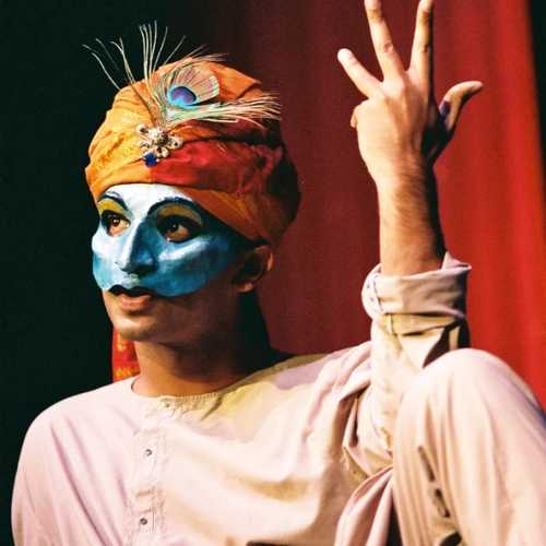 A person with a mask and turban gestures four fingers in the air