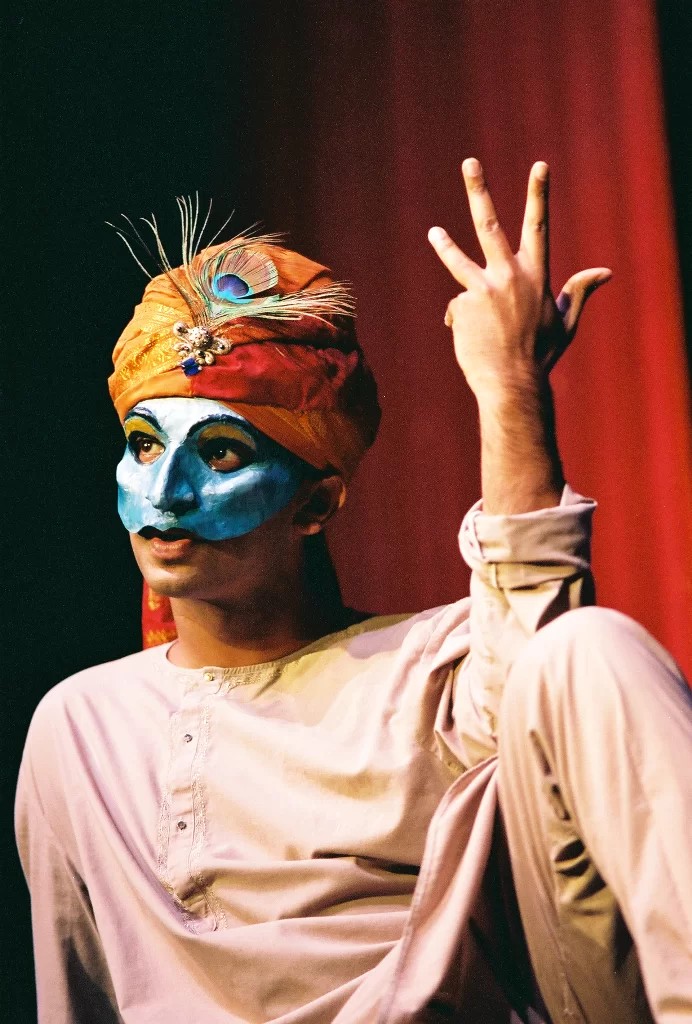 A person with a mask and turban gestures four fingers in the air