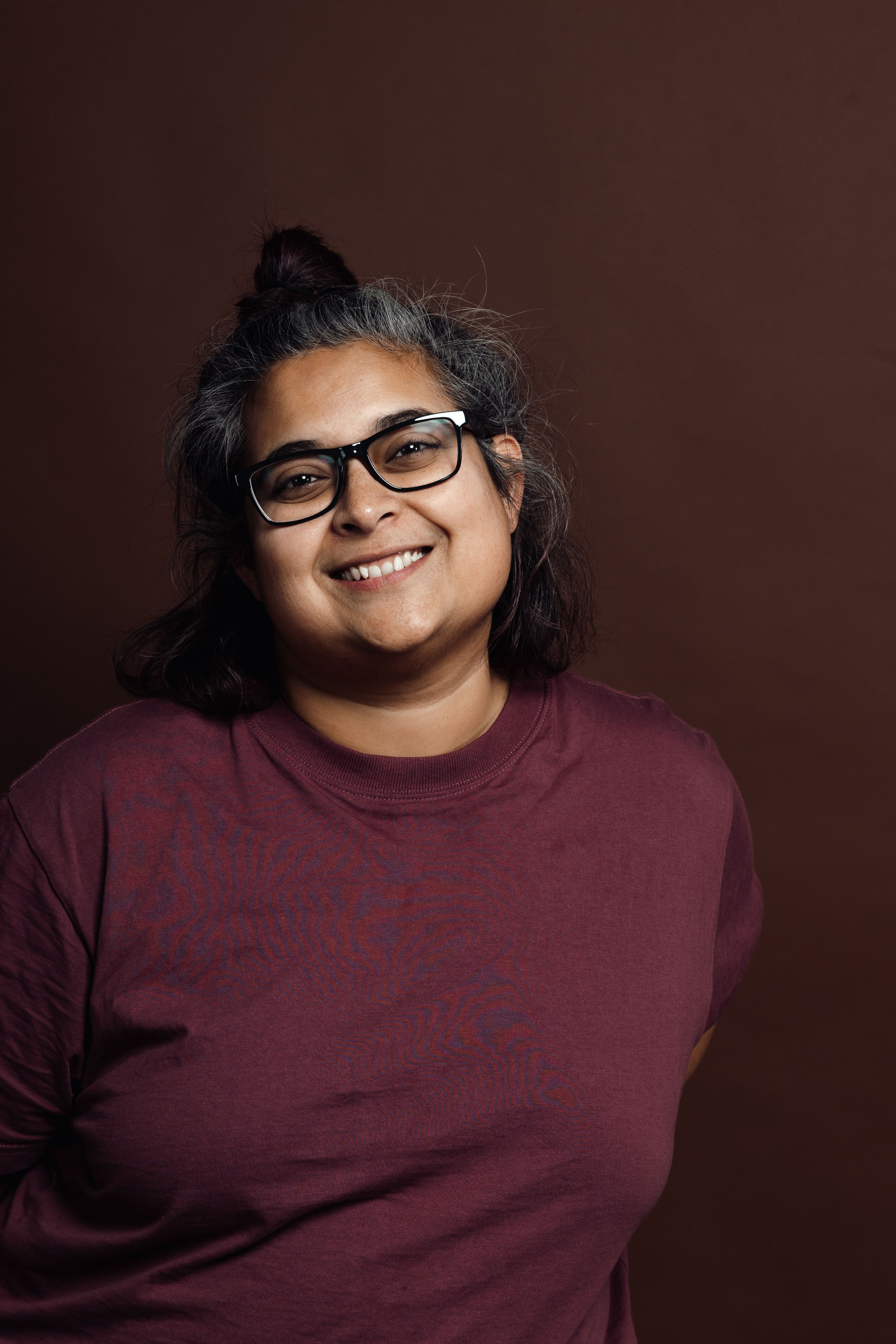 A woman with curly grey hair and glasses smiles with her eyes closed.